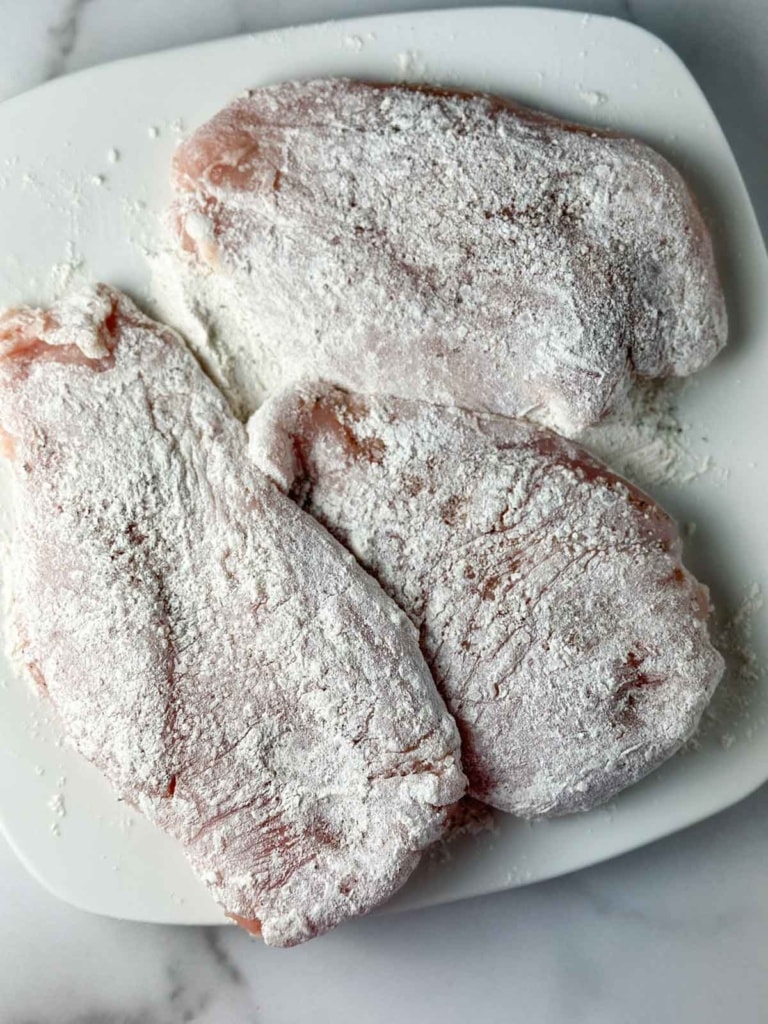 Coating raw chicken in flour.