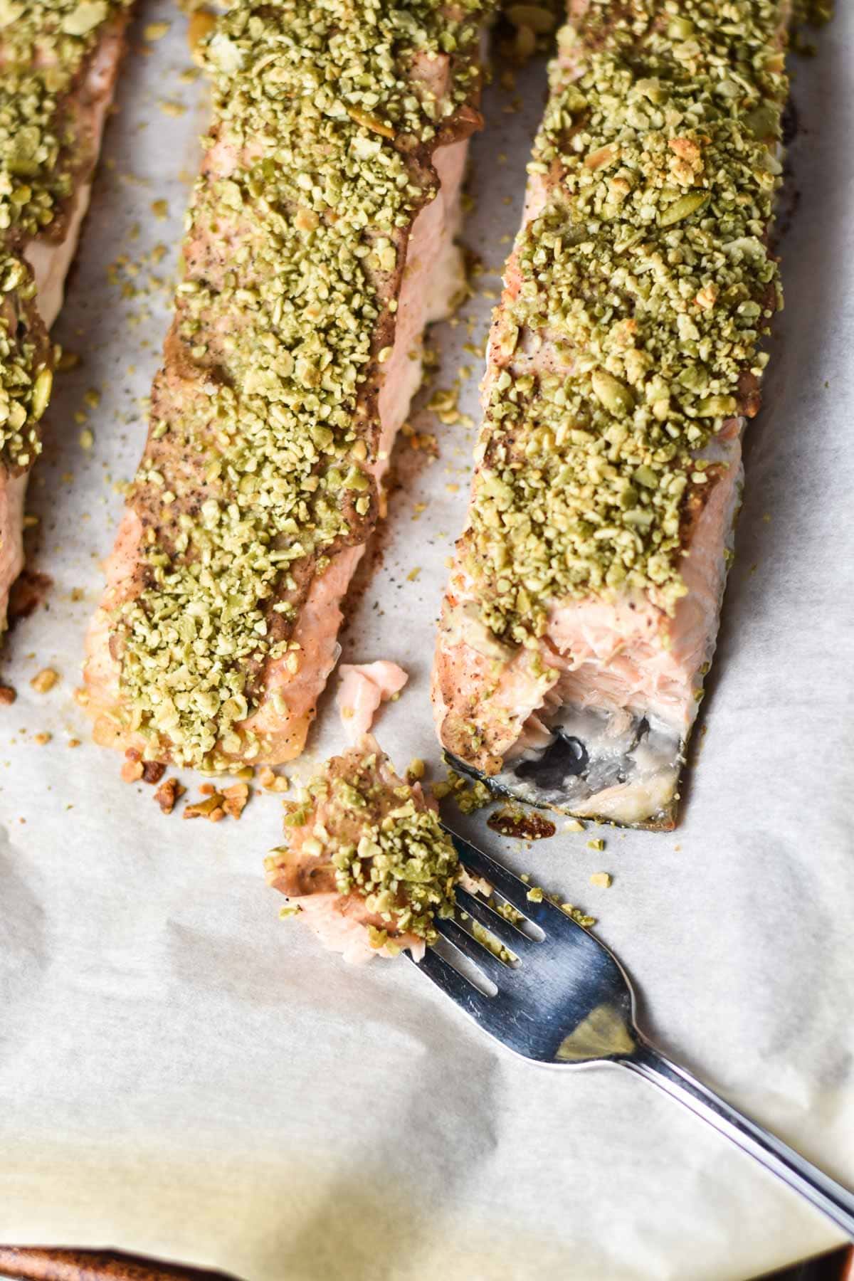 Salmon fillets topped with pepita seeds on a baking sheet.