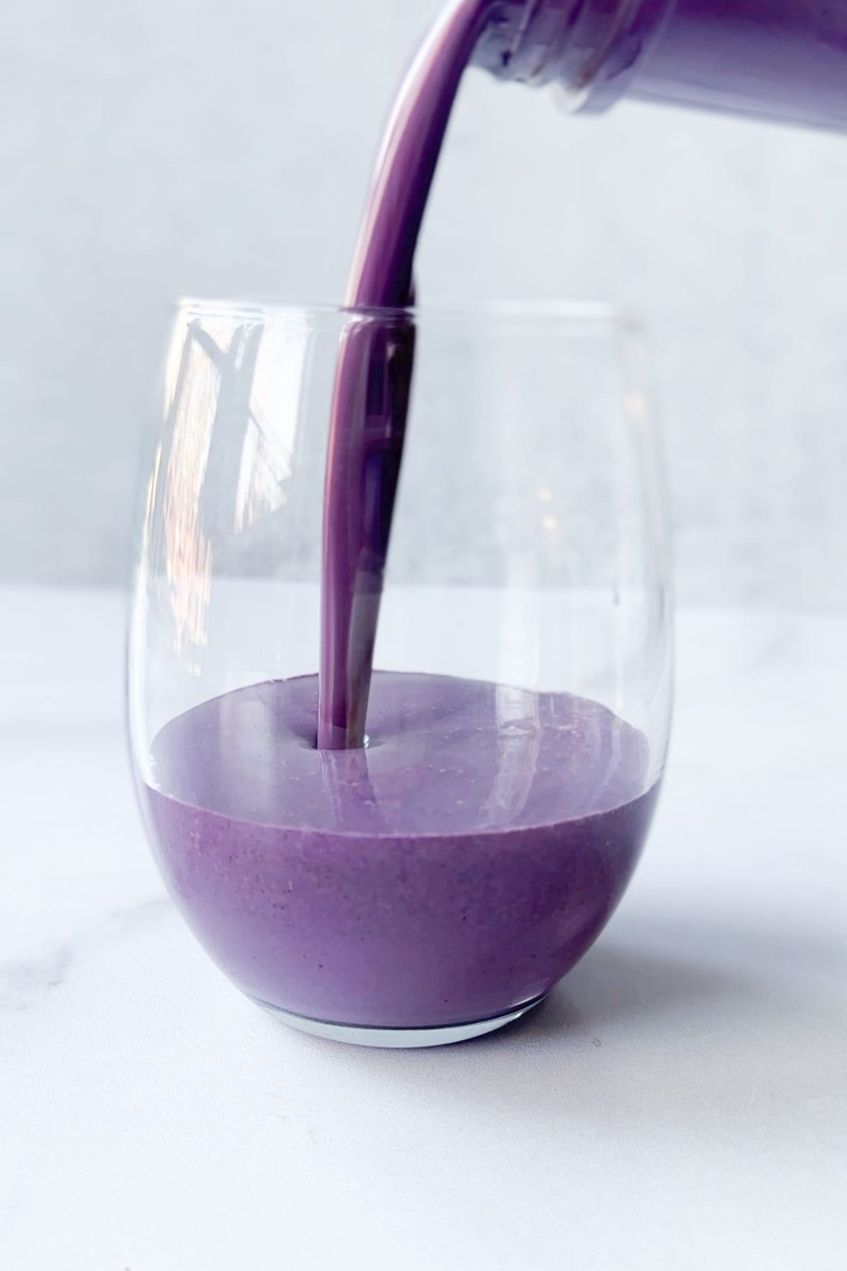 The blueberry smoothie all blended together being poured into a glass.