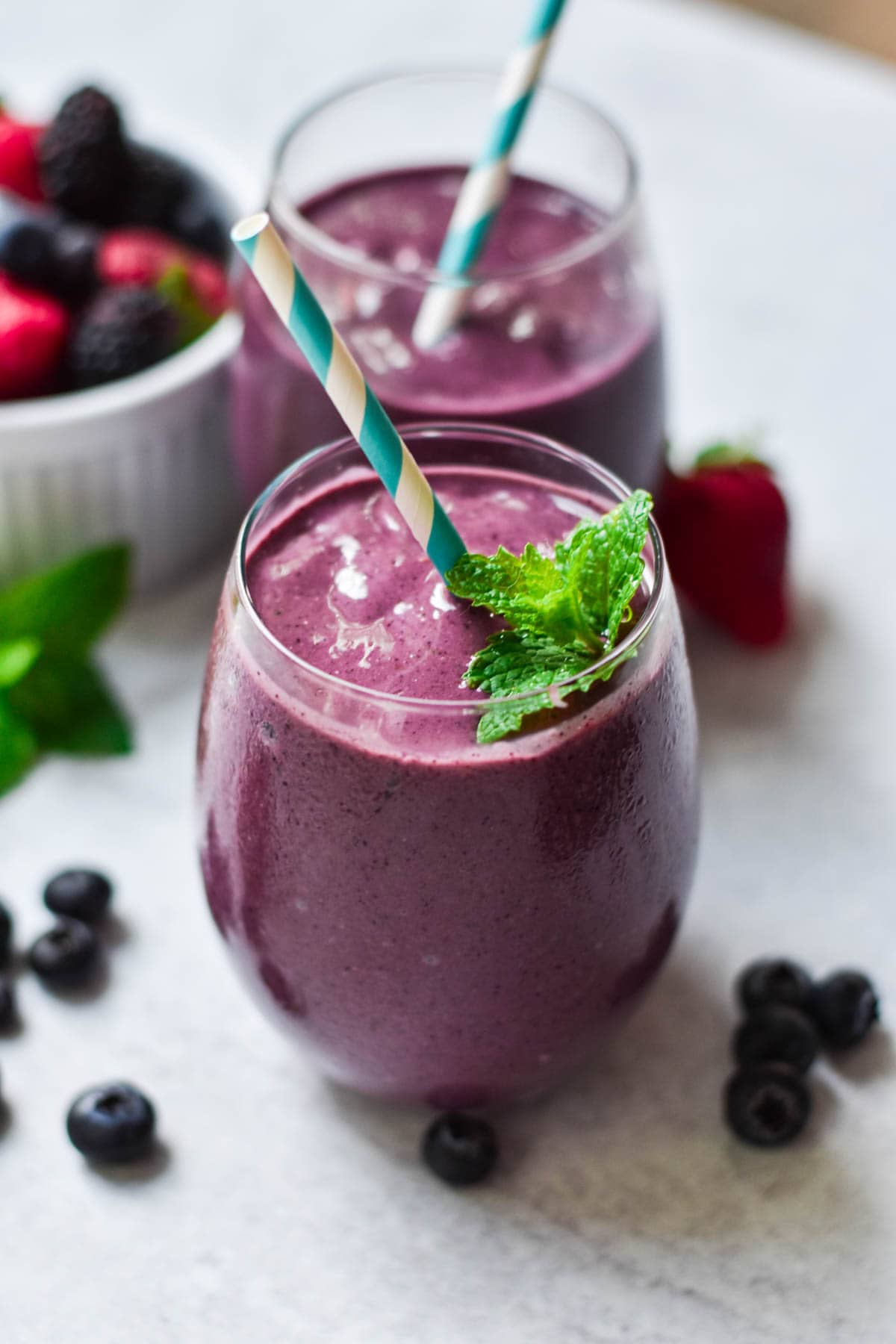 Two berry smoothies with mint on top and mixed berries on the table.