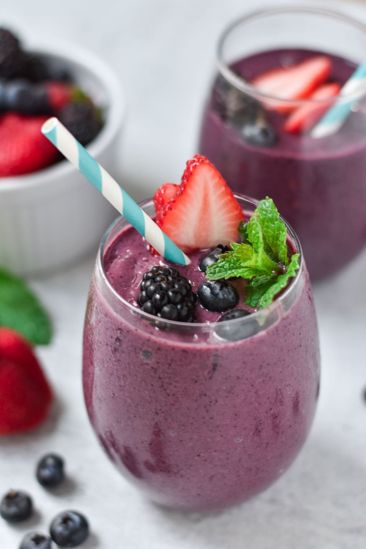 Two berry smoothies next to a bowl of mixed berries.
