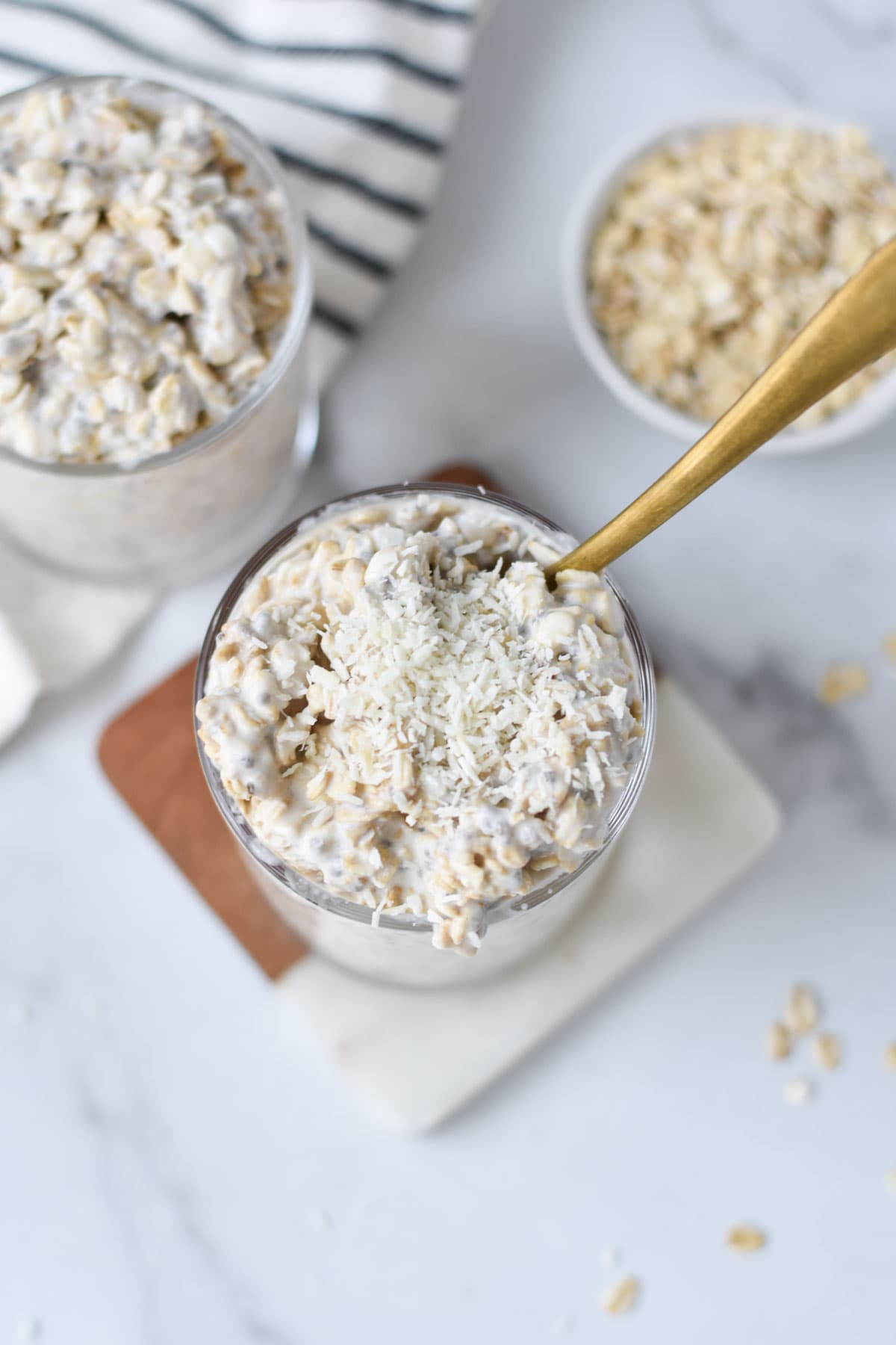 Overnight oats in jars with coconut and oats on a table.