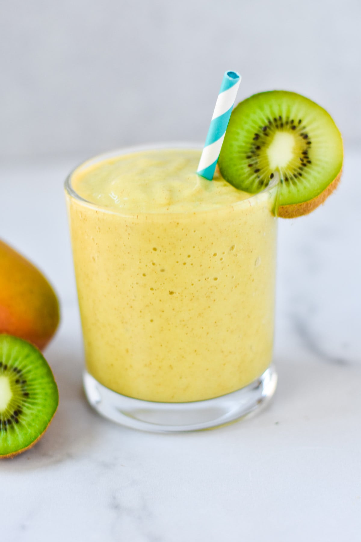 A yellow smoothie in a short glass with a kiwi on the rim.
