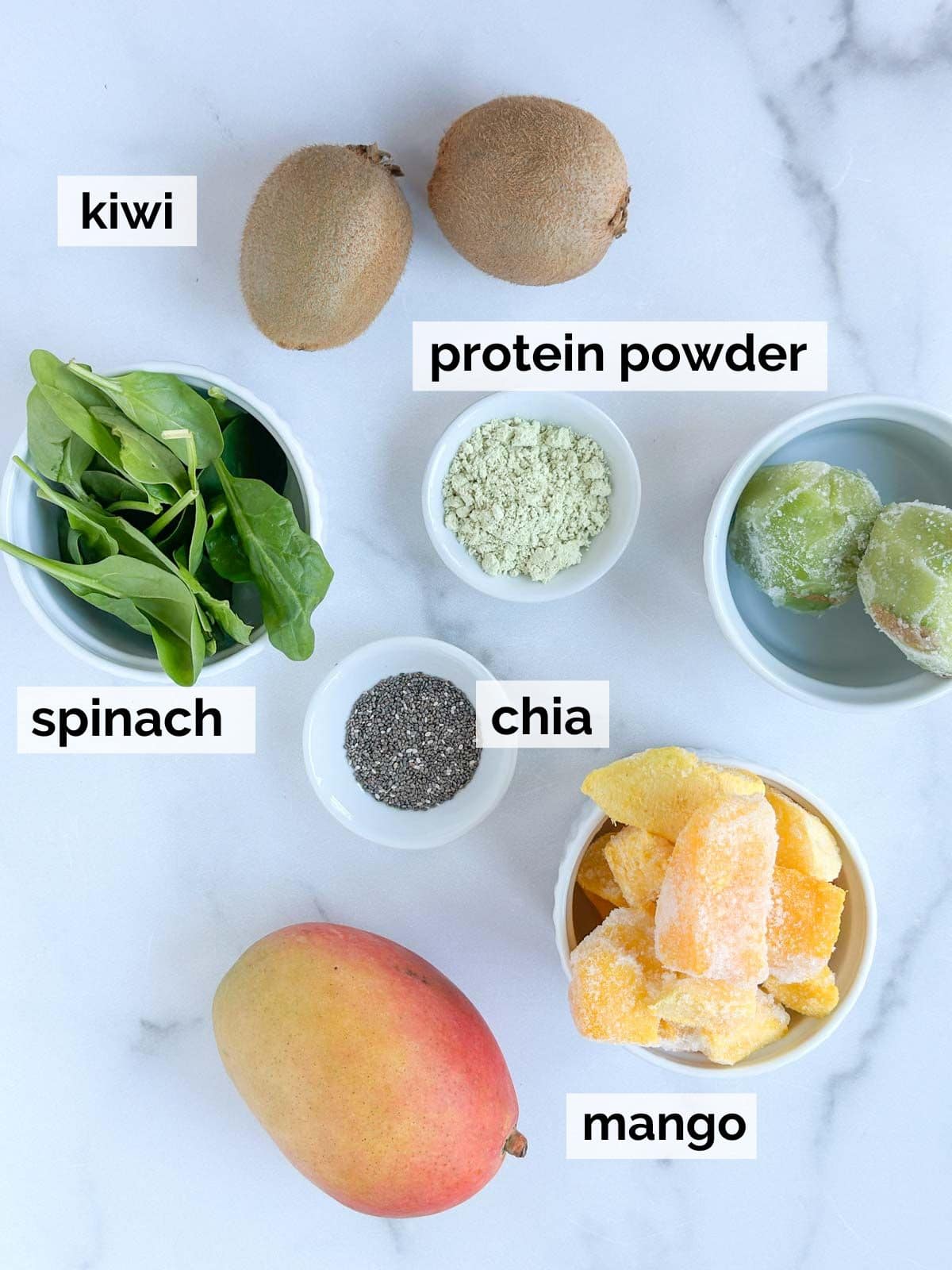 Ingredients for a mango kiwi smoothie on a white marble background.