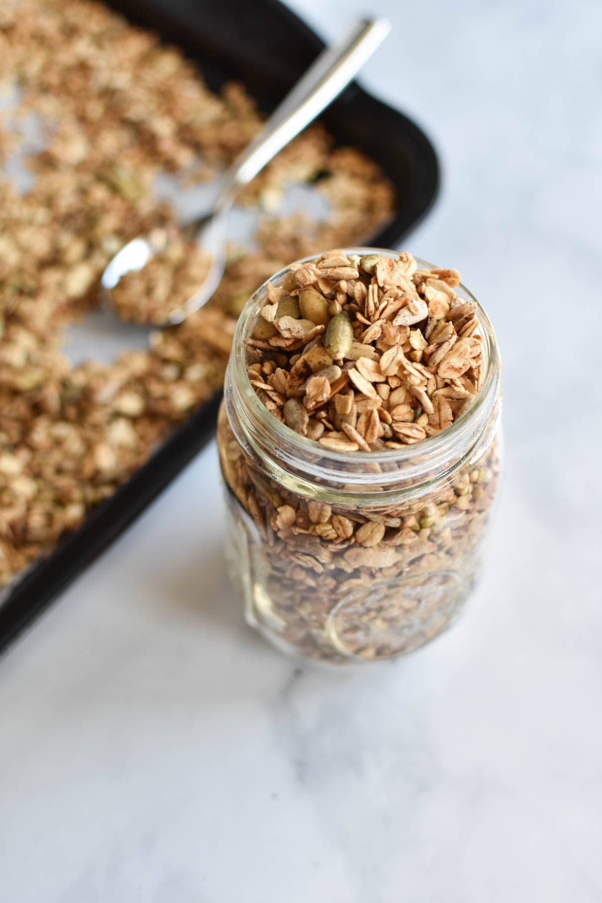 Granola in a mason jar next to a baking sheet with a spoon.