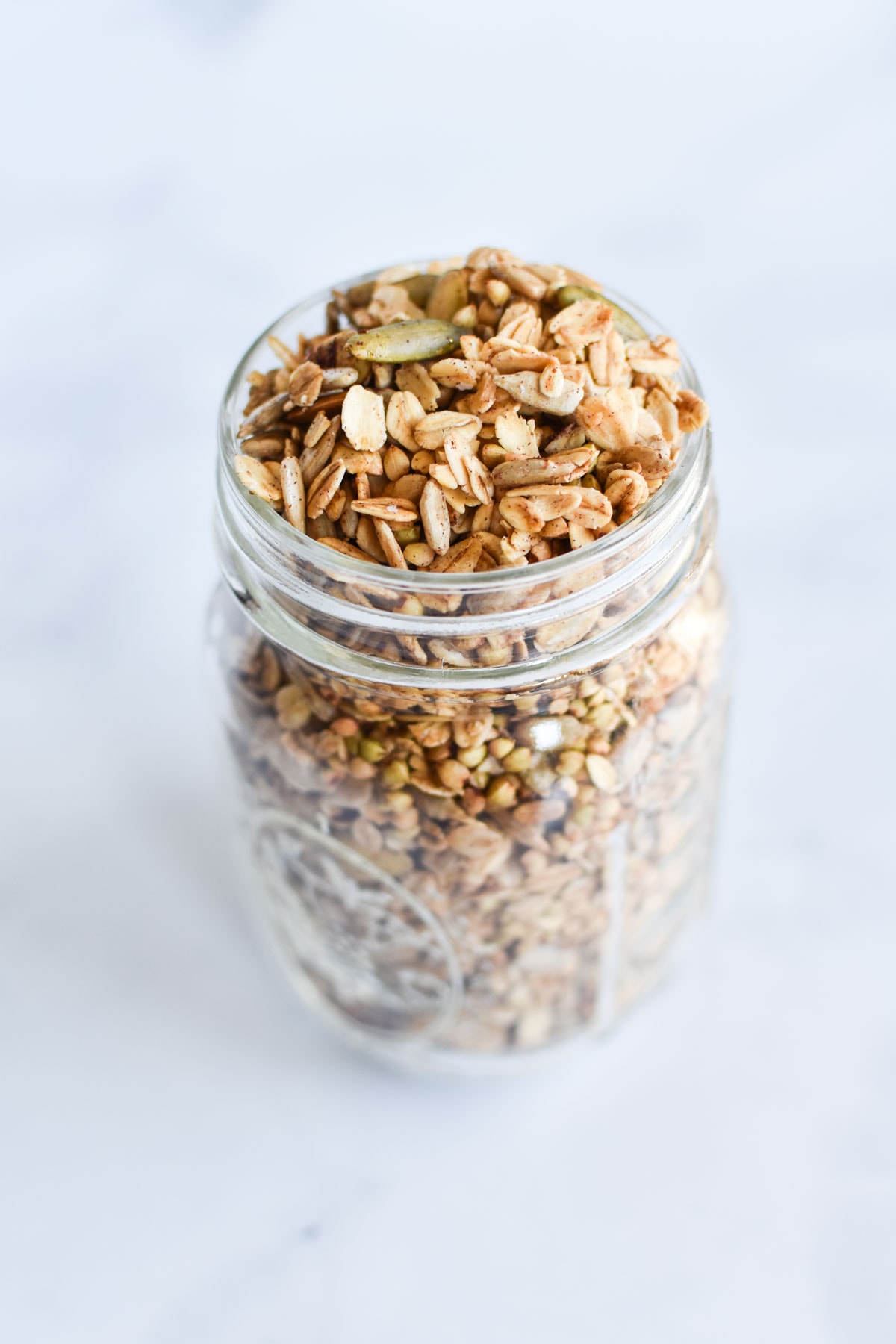 Granola in a mason jar on a white table.