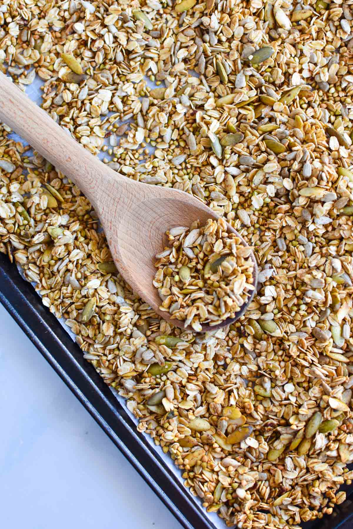 Granola being scooped with a wood spoon on a baking sheet.