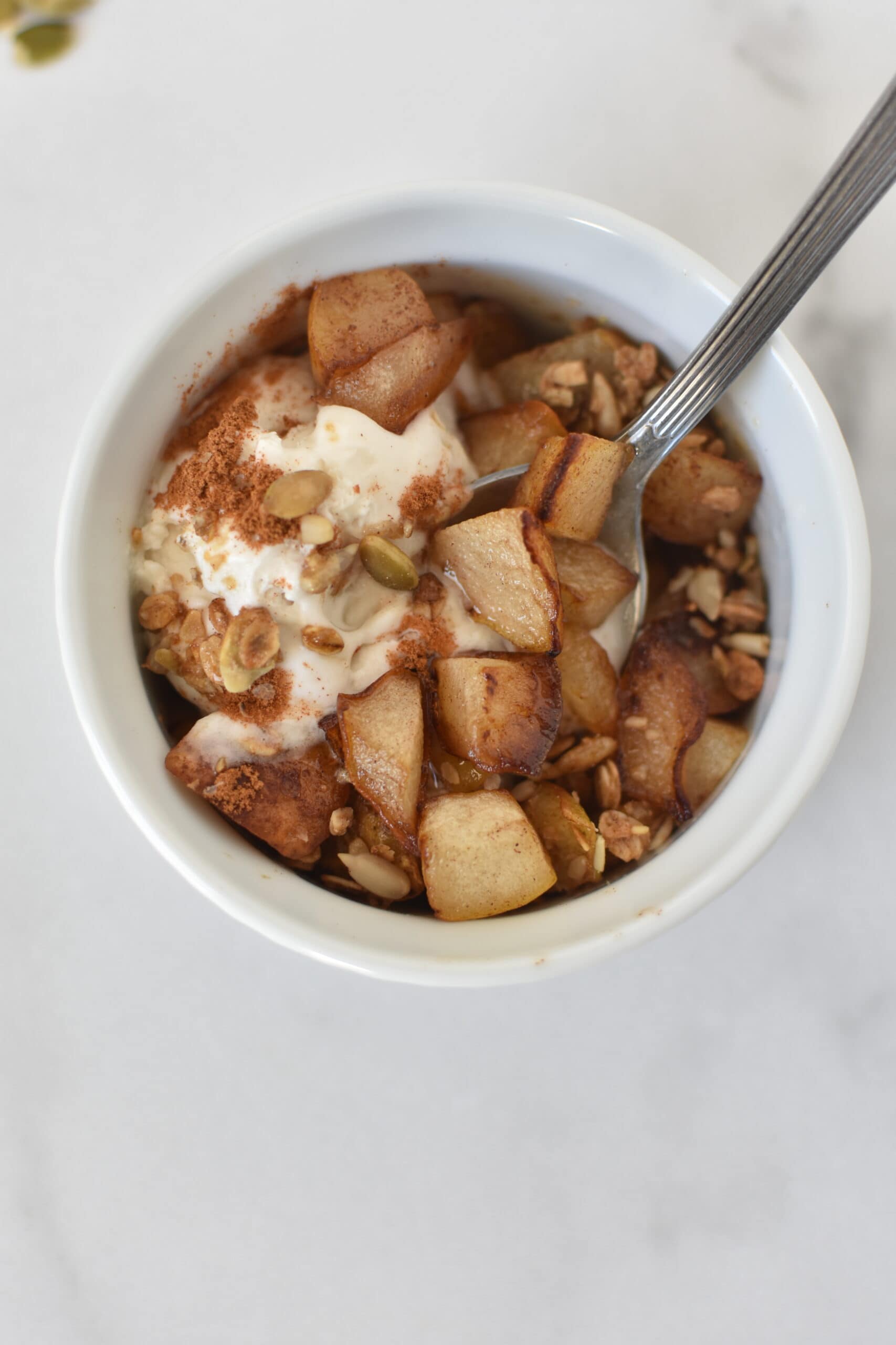 Ice cream and pears topped with granola in a white bowl.