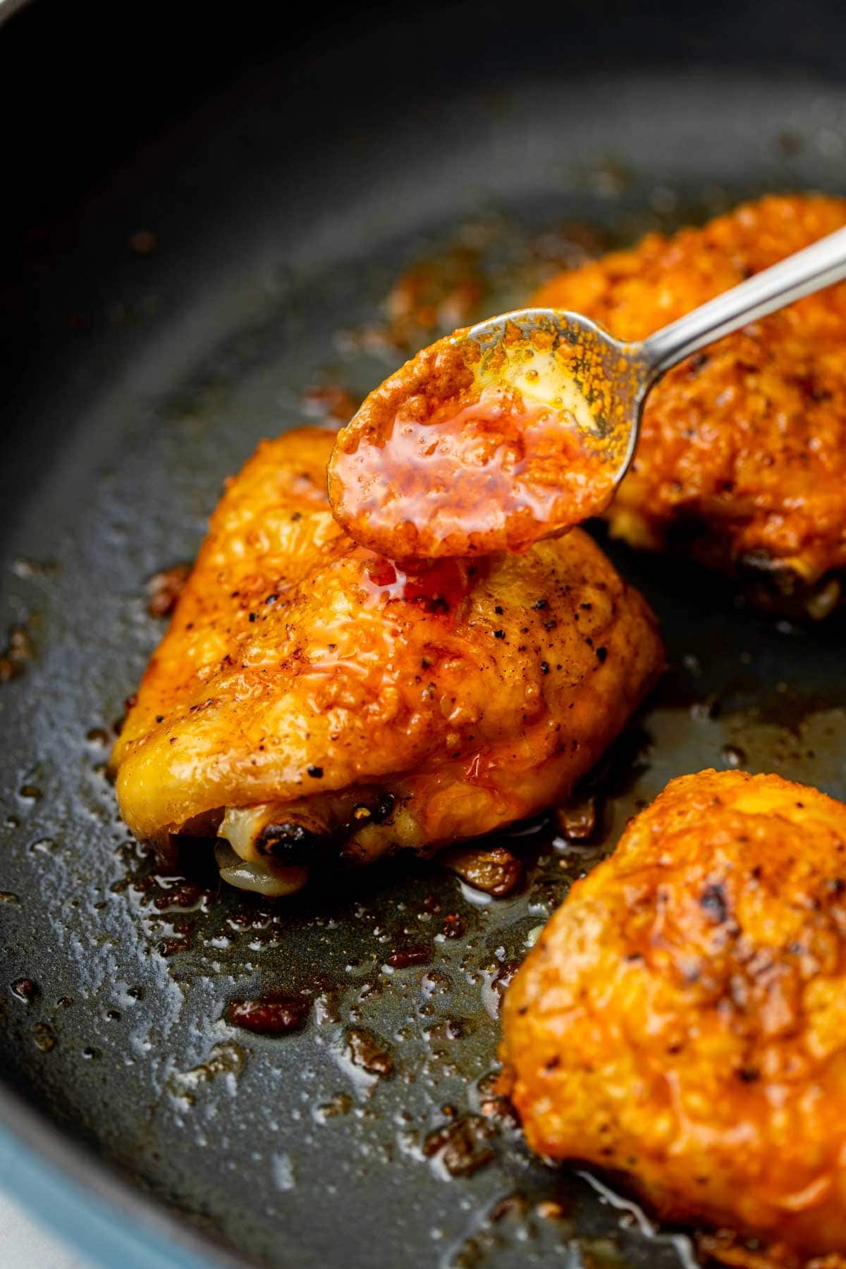 Spooning buffalo sauce over a pan-fried chicken thigh.