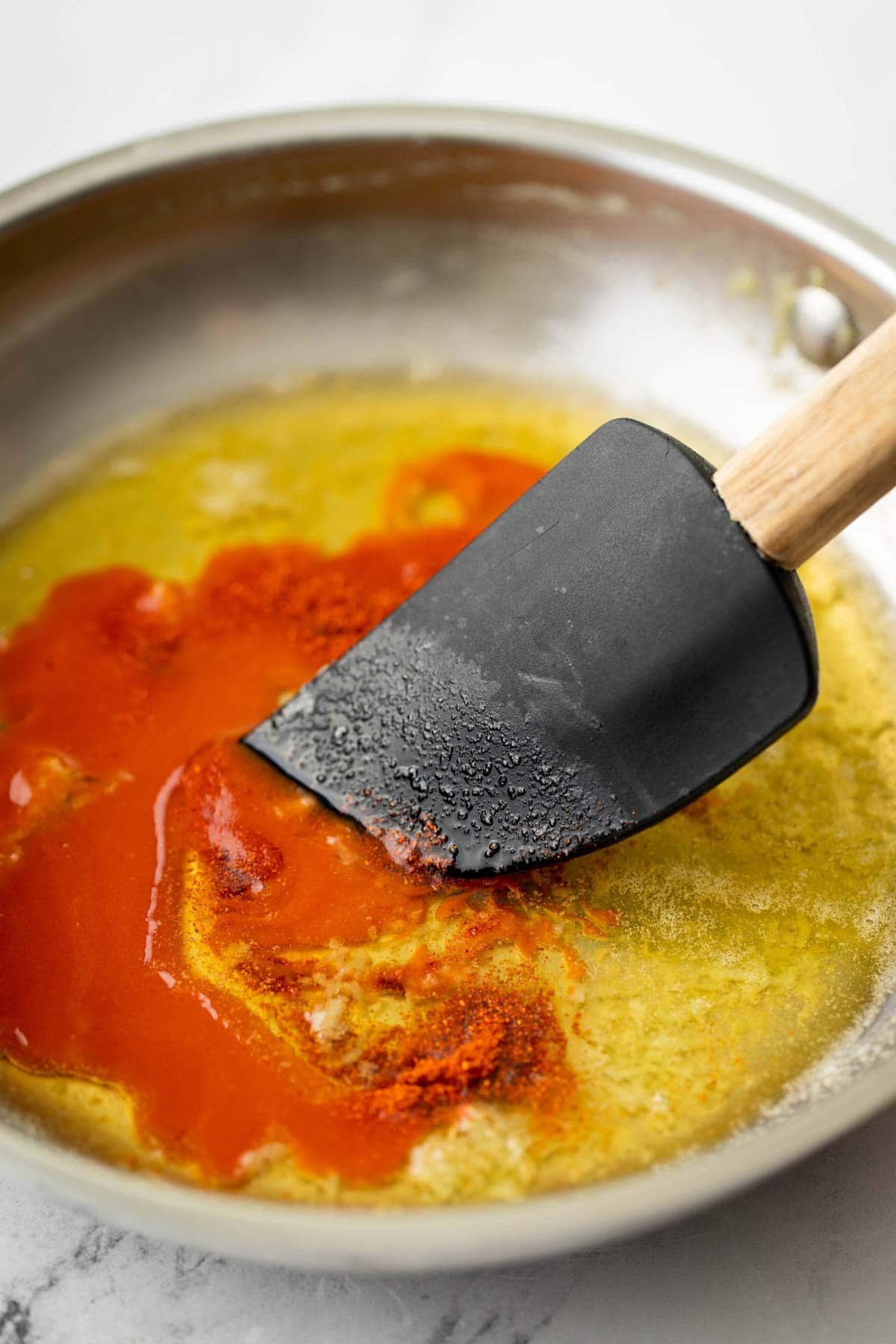 Adding buffalo sauce to a pan with butter and garlic.