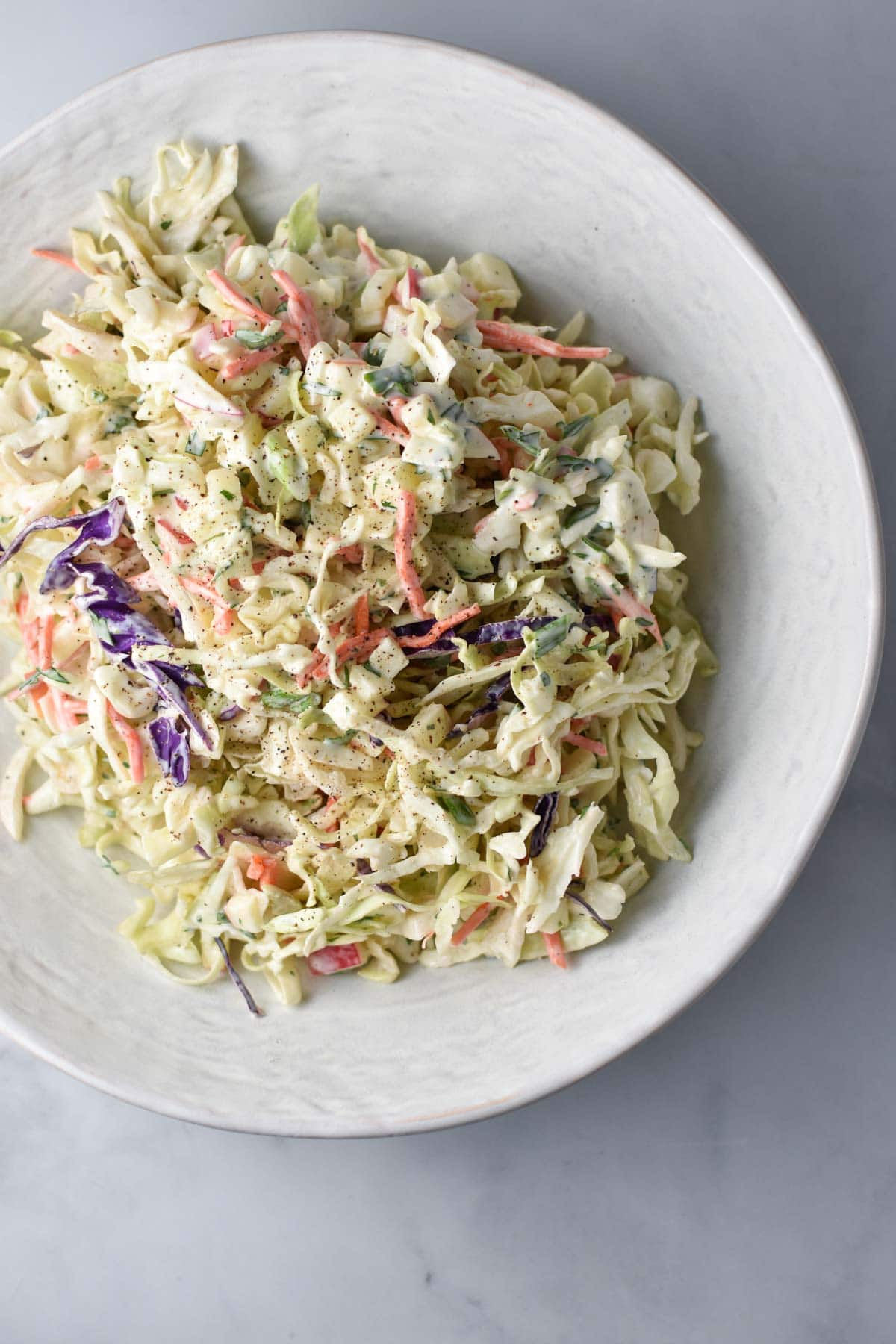 Creamy coleslaw in a white bowl on a white table.