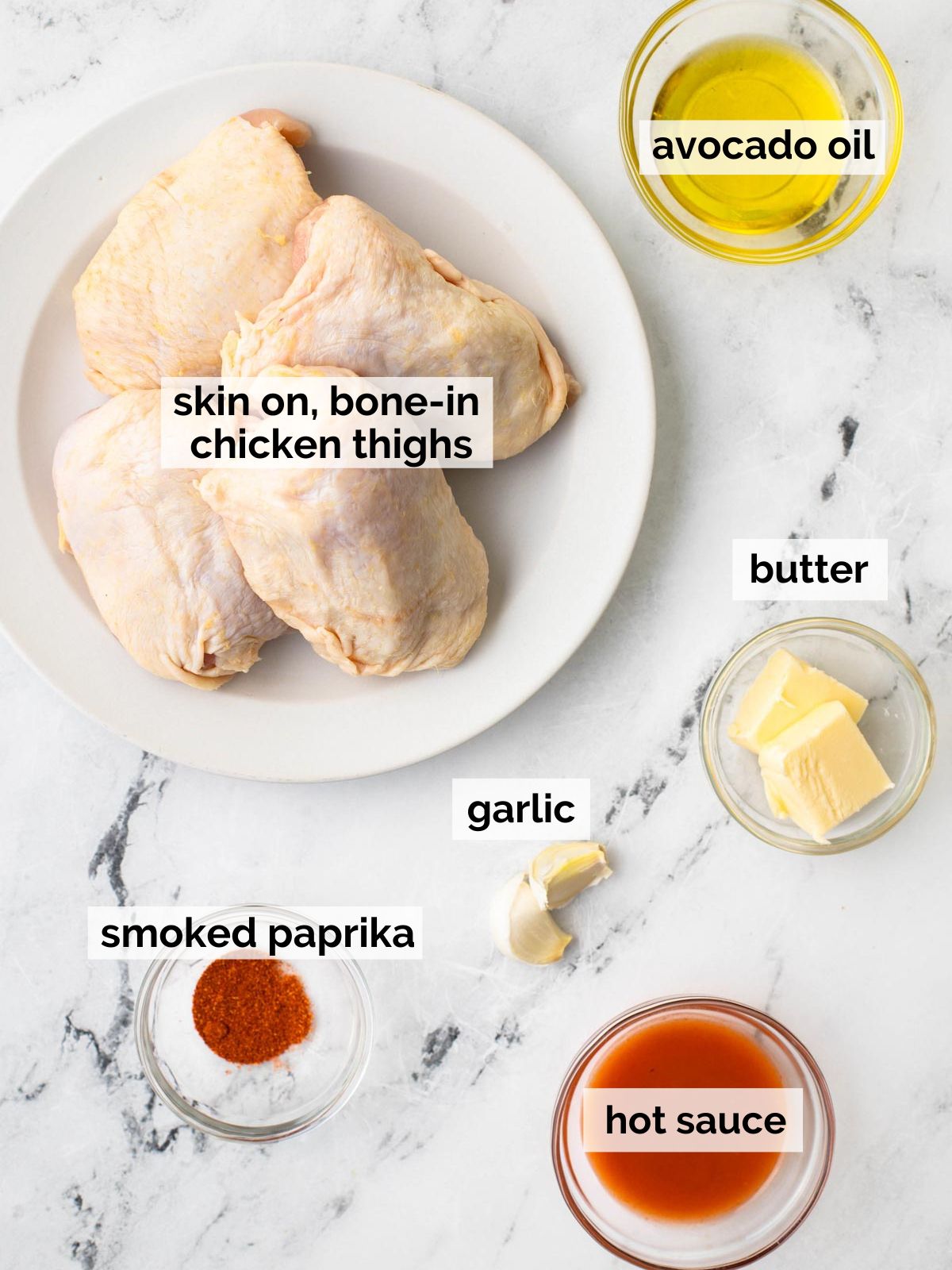 Ingredients for buffalo chicken thighs on a white marble table.