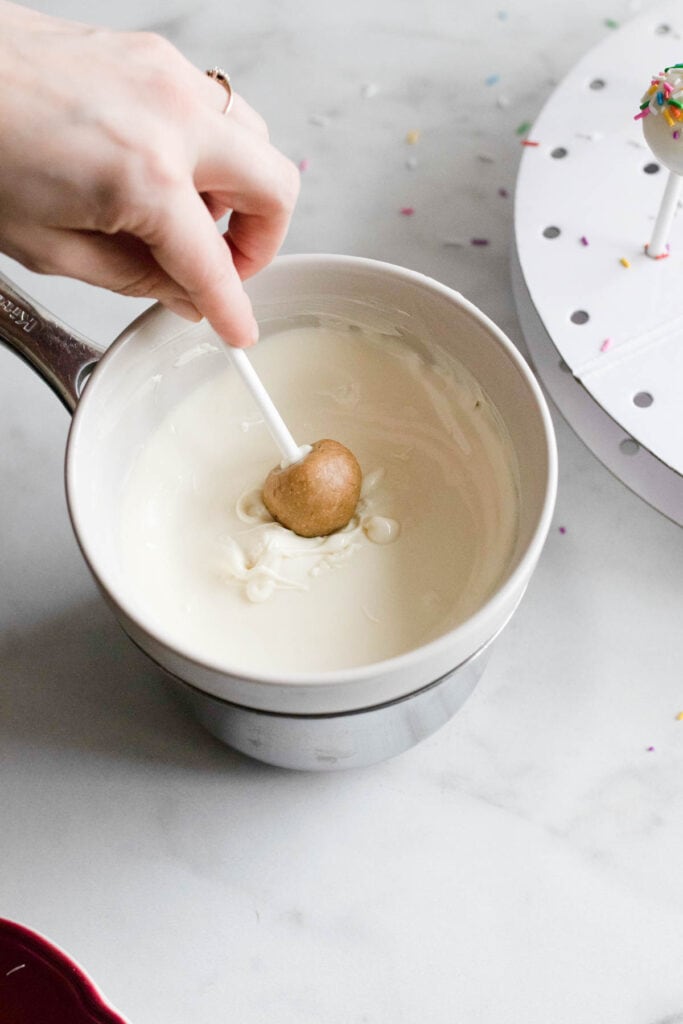 A hand dipping a cake pop into white chocolate. 