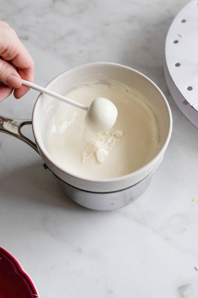 A hand removing the cake pop coated in white chocolate.