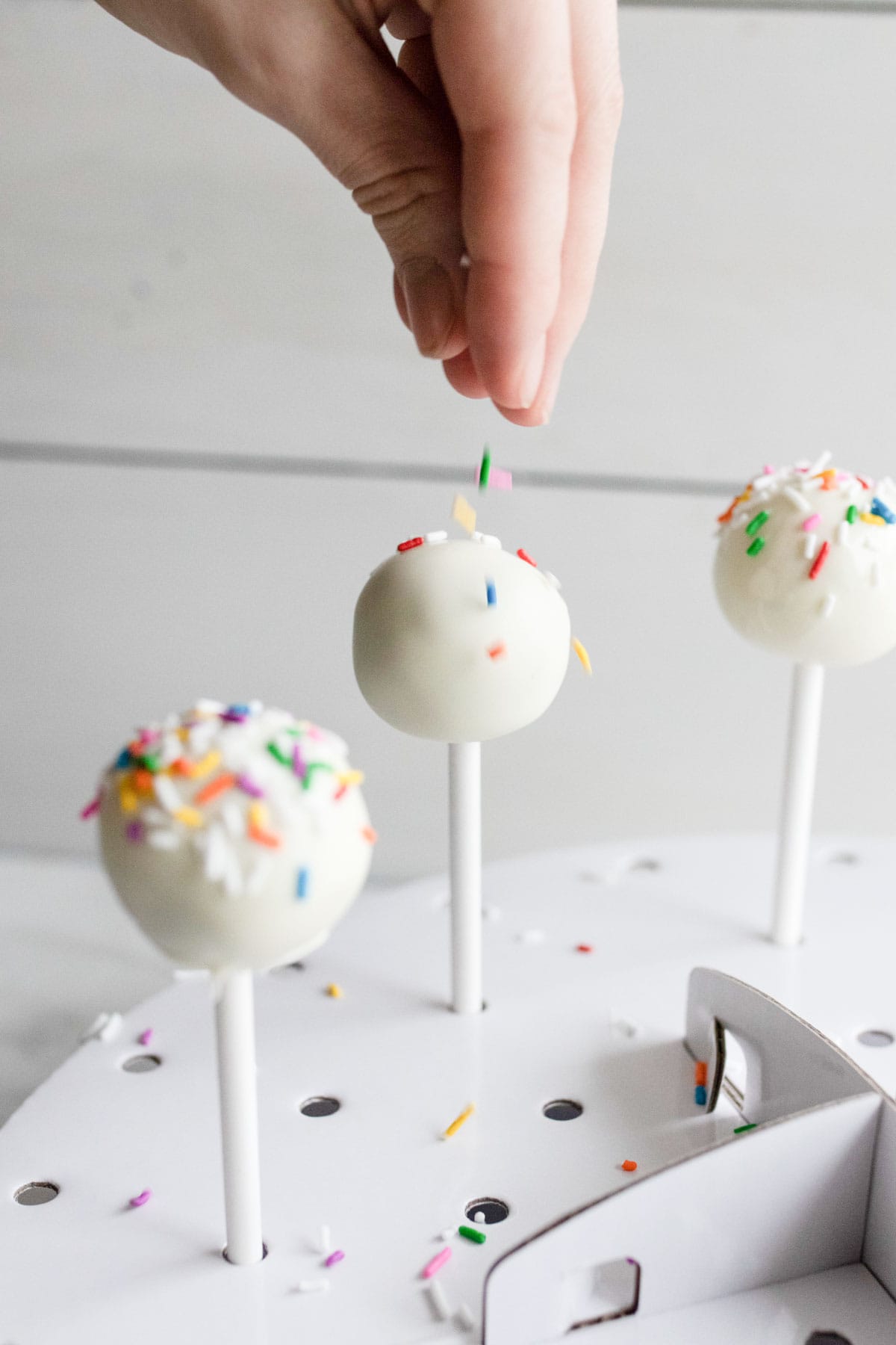 Adding sprinkles on top of a cake pop. 