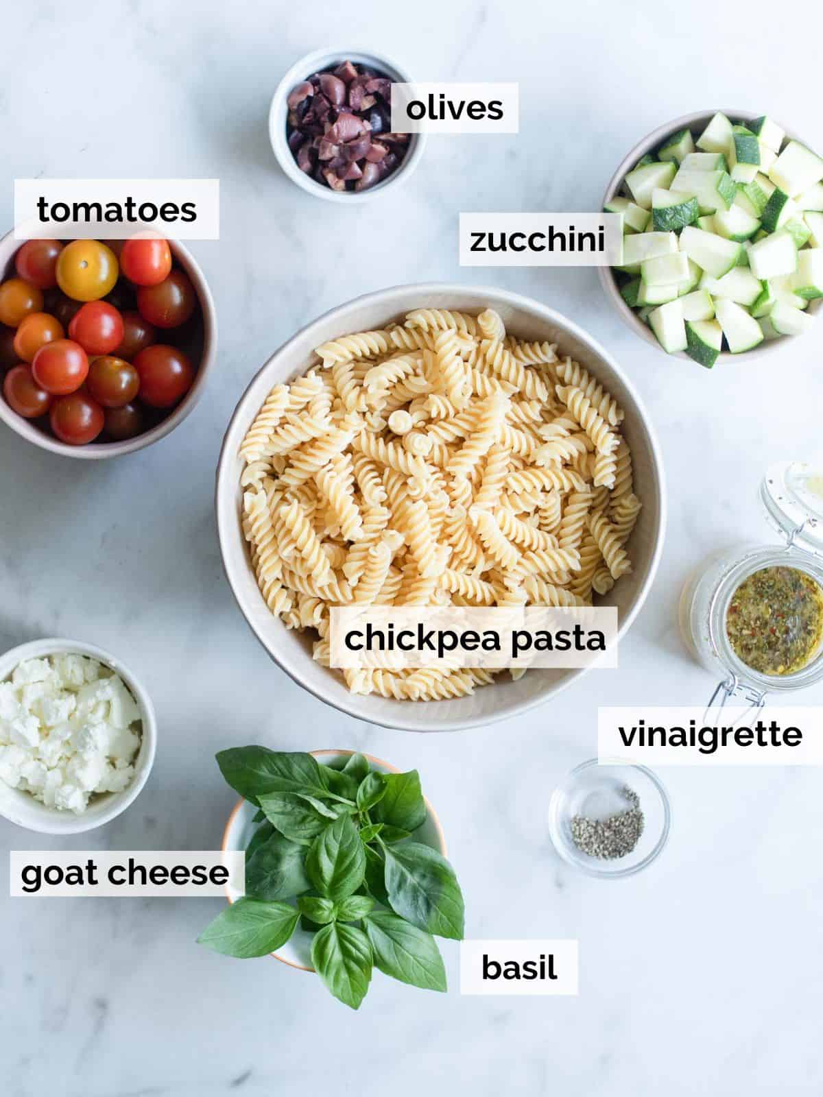 Ingredients for chickpea pasta salad on a white marble background.