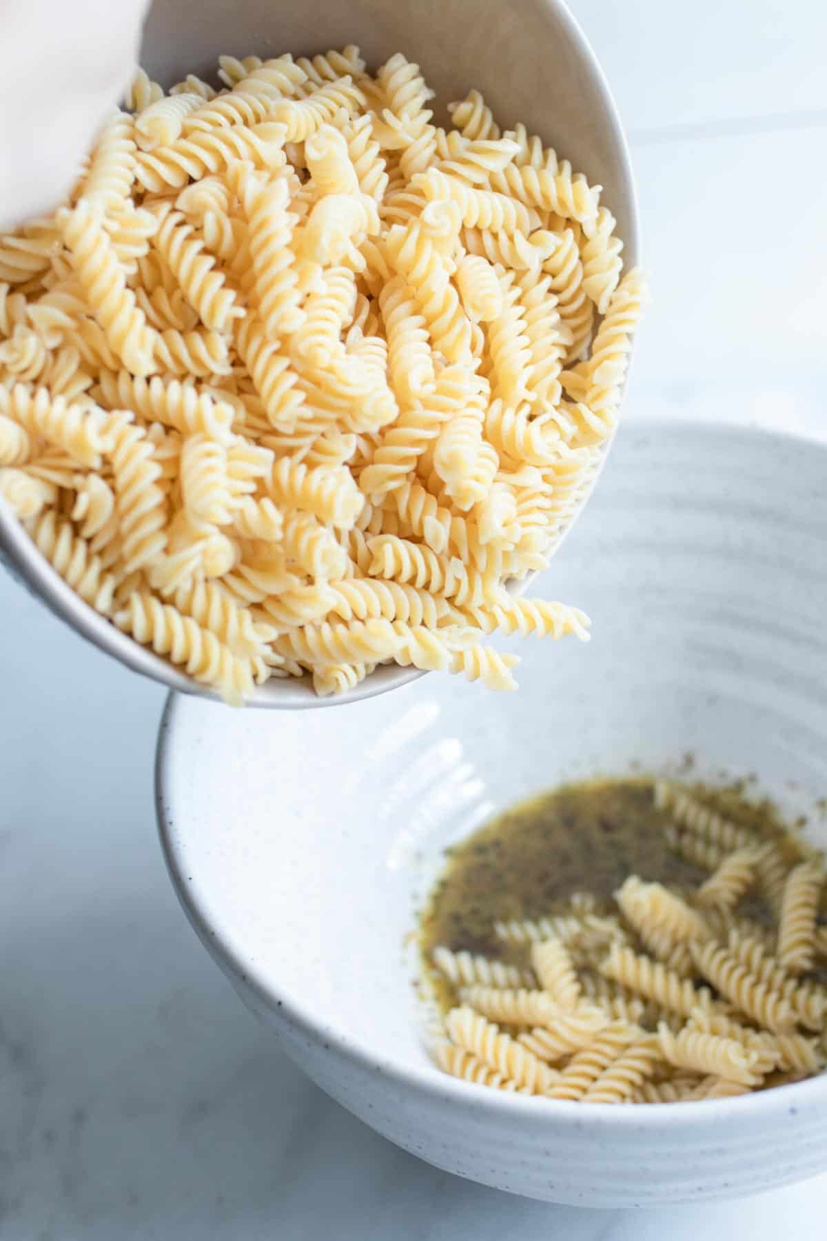 Pouring pasta into a bowl of dressing.