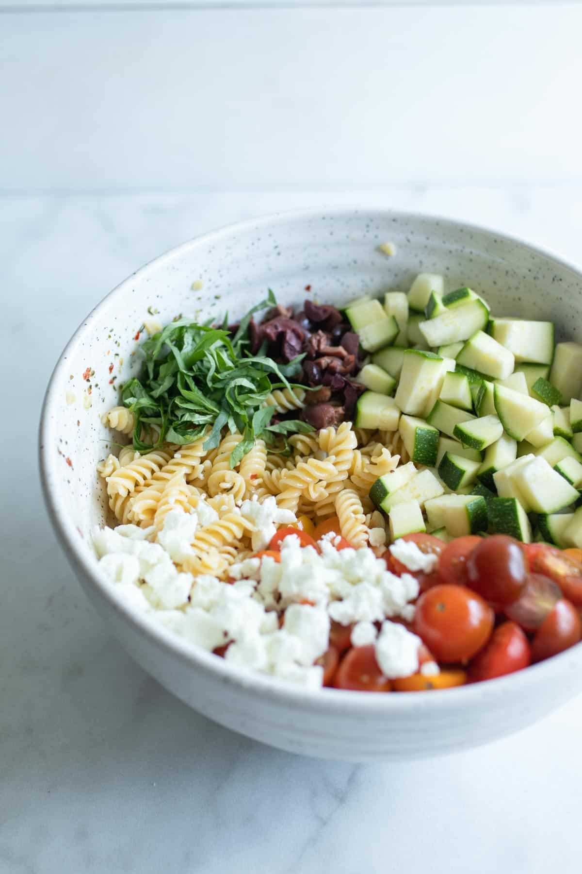 Pasta, goat cheese, tomatoes, basil, and zucchini in a bowl.