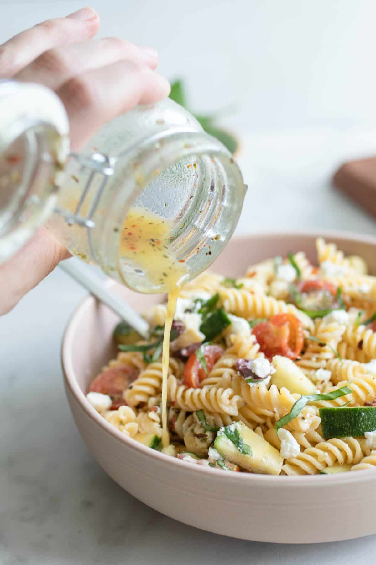 Pouring dressing onto a Mediterranean pasta salad.