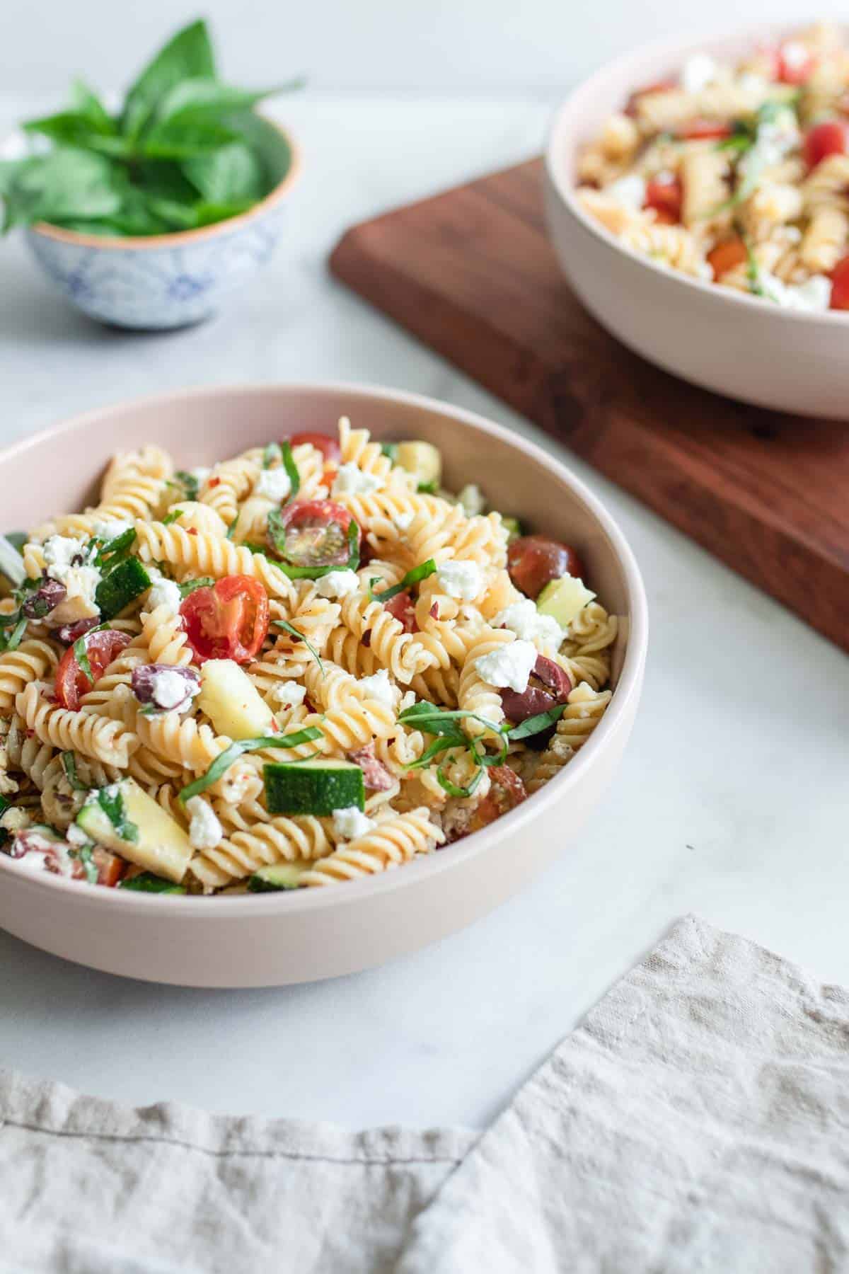 Two bowls of vegetable pasta salad topped with zucchini and tomatoes.