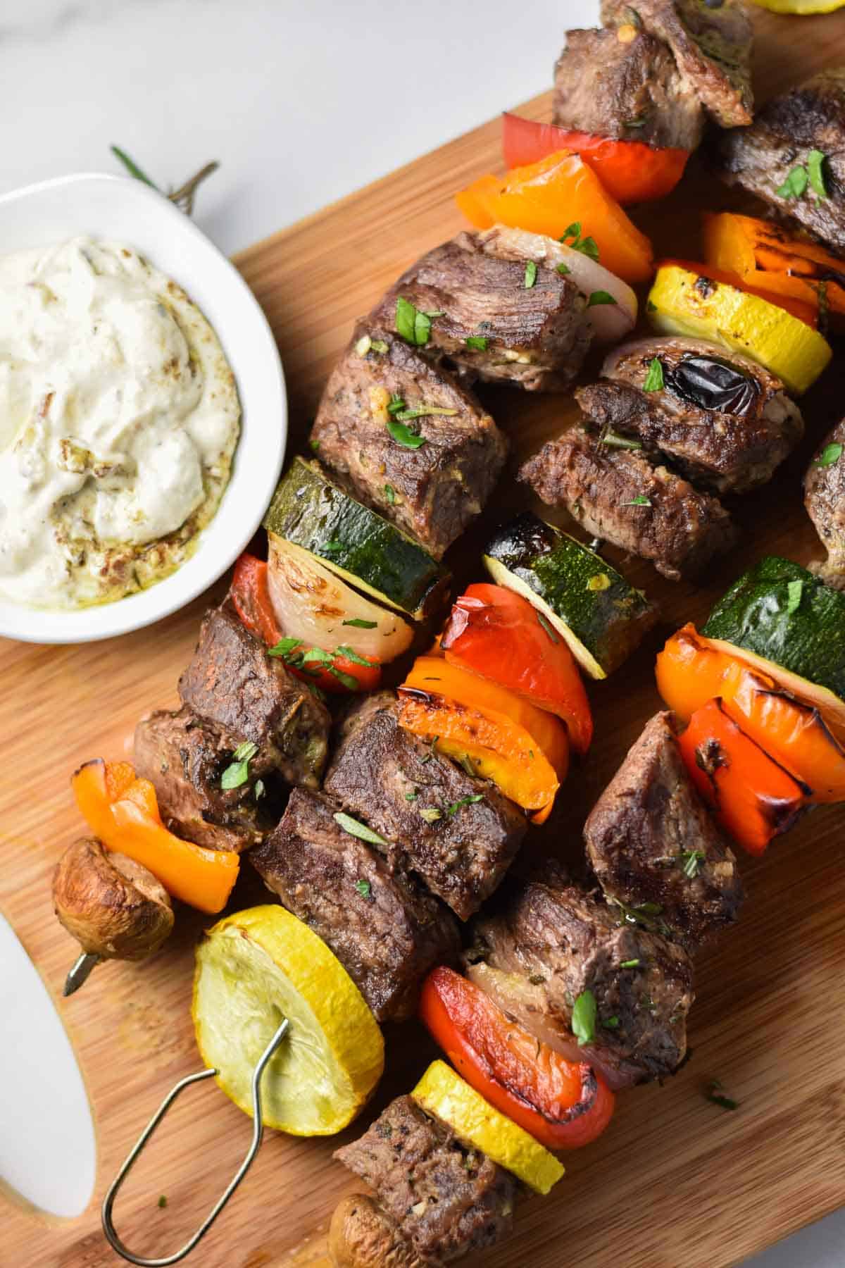 Beef kebobs next to a bowl of zucchini and cottage cheese whipped dip.