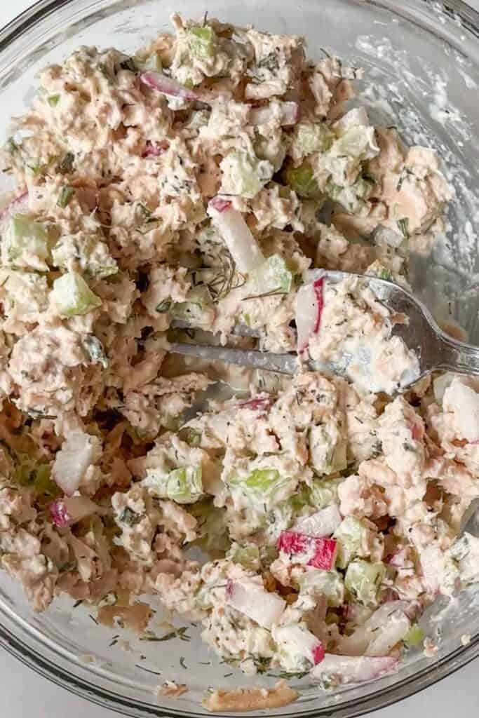 Tuna salad being mixed together in a glass bowl.