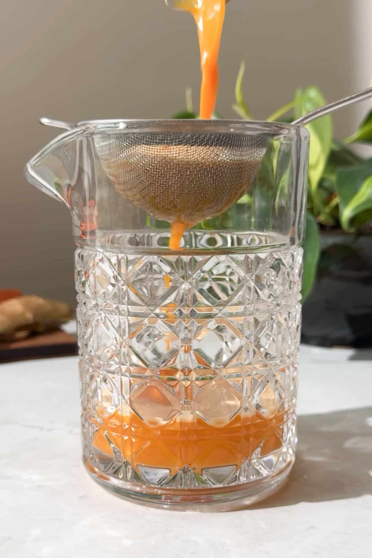 Pouring wellness shots through a fine mesh strainer after blending.