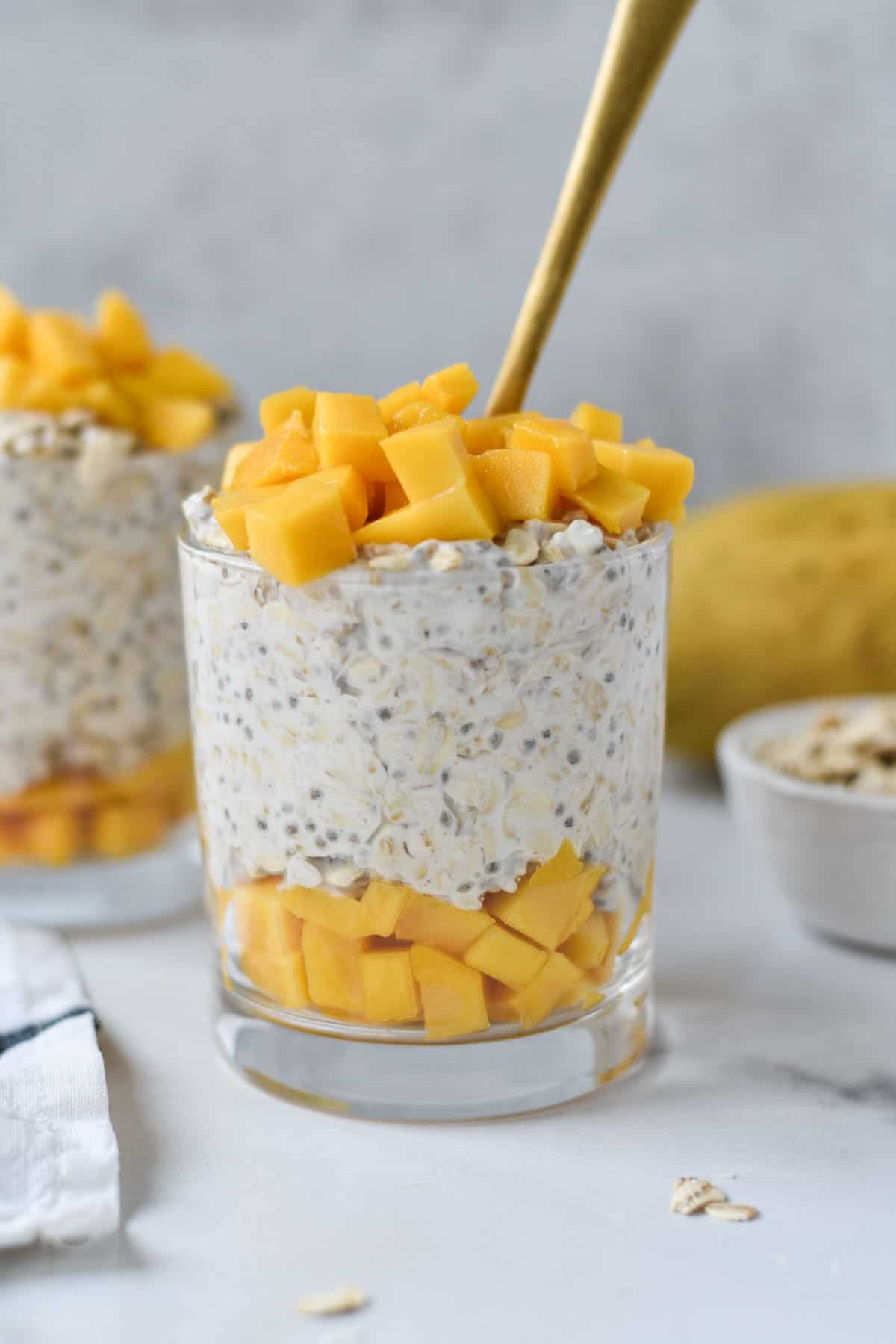 A jar of mango and coconut overnight oats topped with fresh sliced mango.
