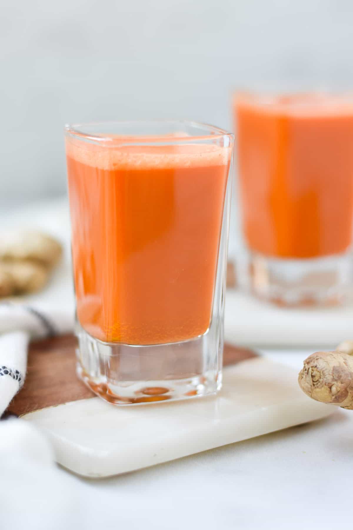 To orange colored shots on a table topped with ginger. 