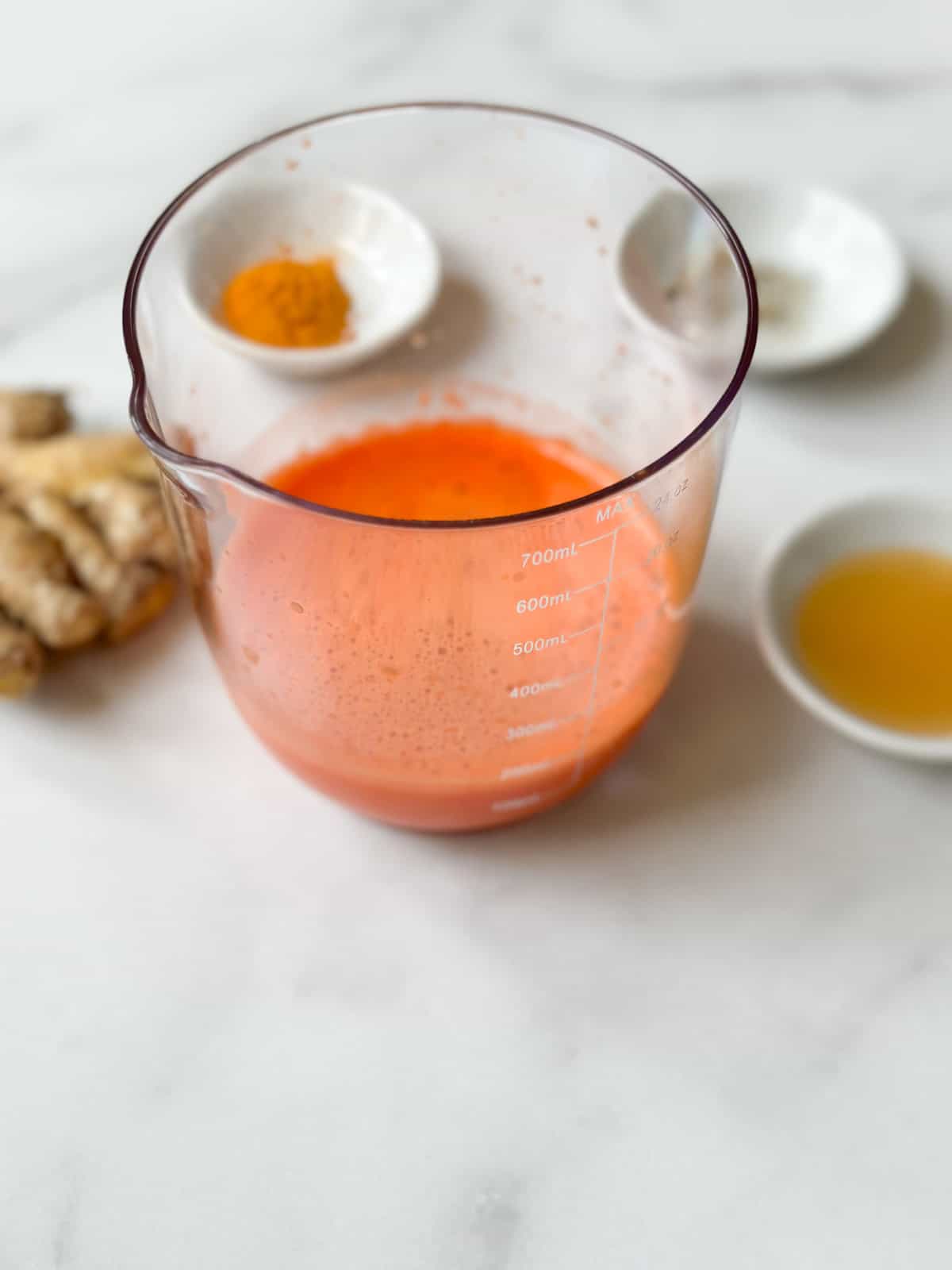 A juicer container of carrot juice next to ginger.