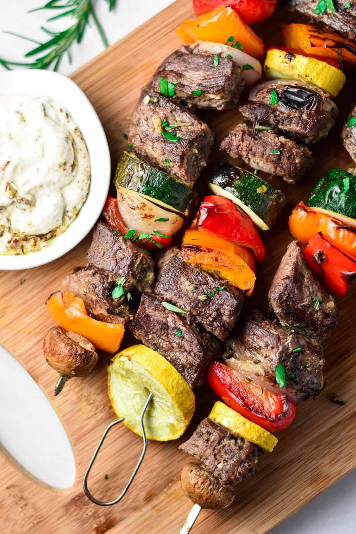 Beef kabobs on a wood cutting board next to a whipped garlic dip.