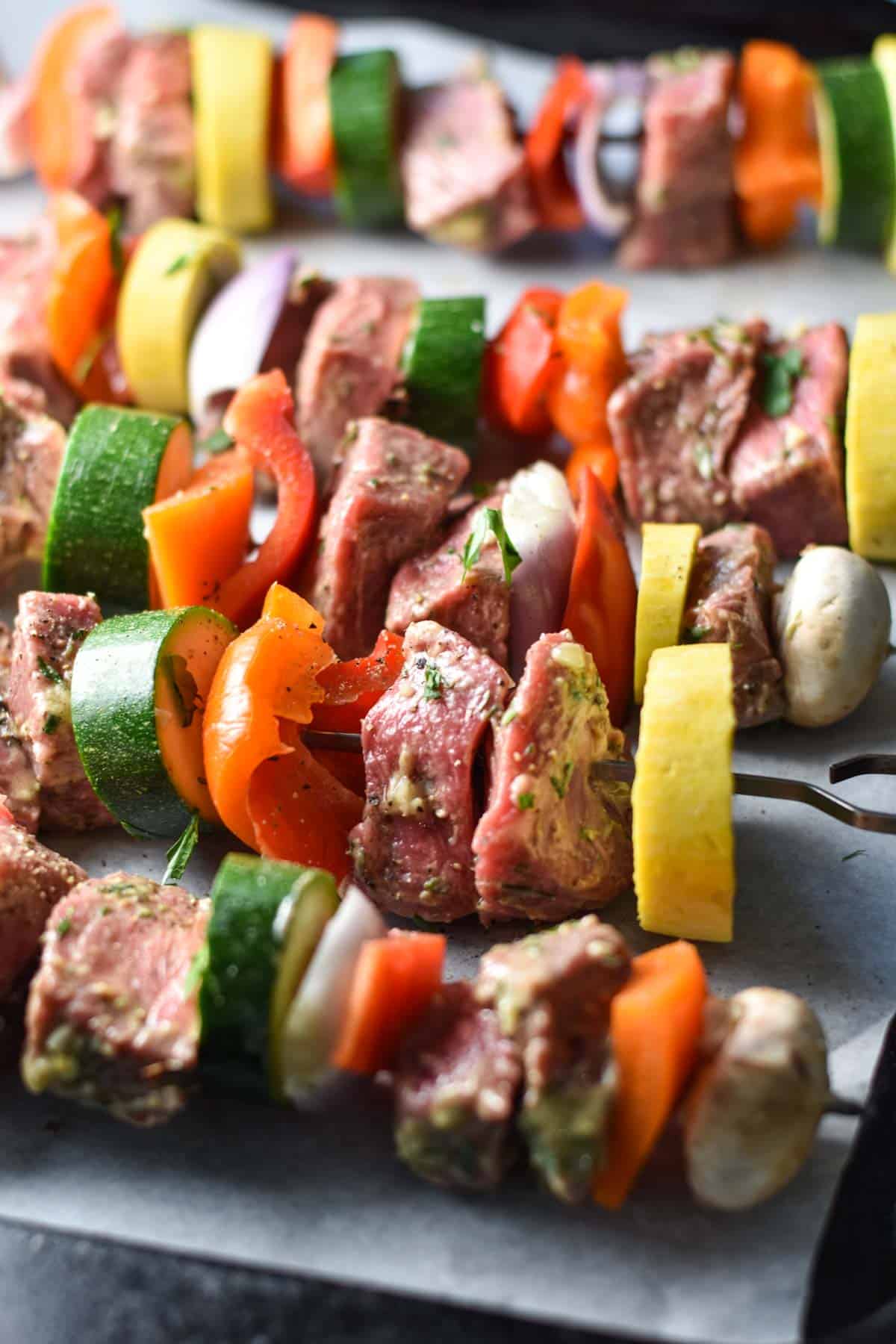Layered vegetables and beef on skewers on a metal sheet pan.
