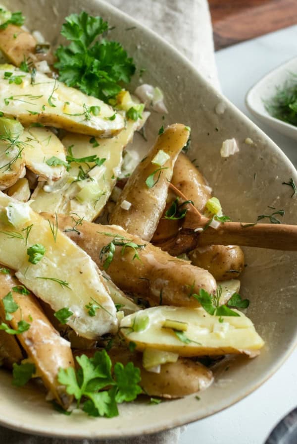 Fingerling potato salad in a beige bowl with a wood spoon.