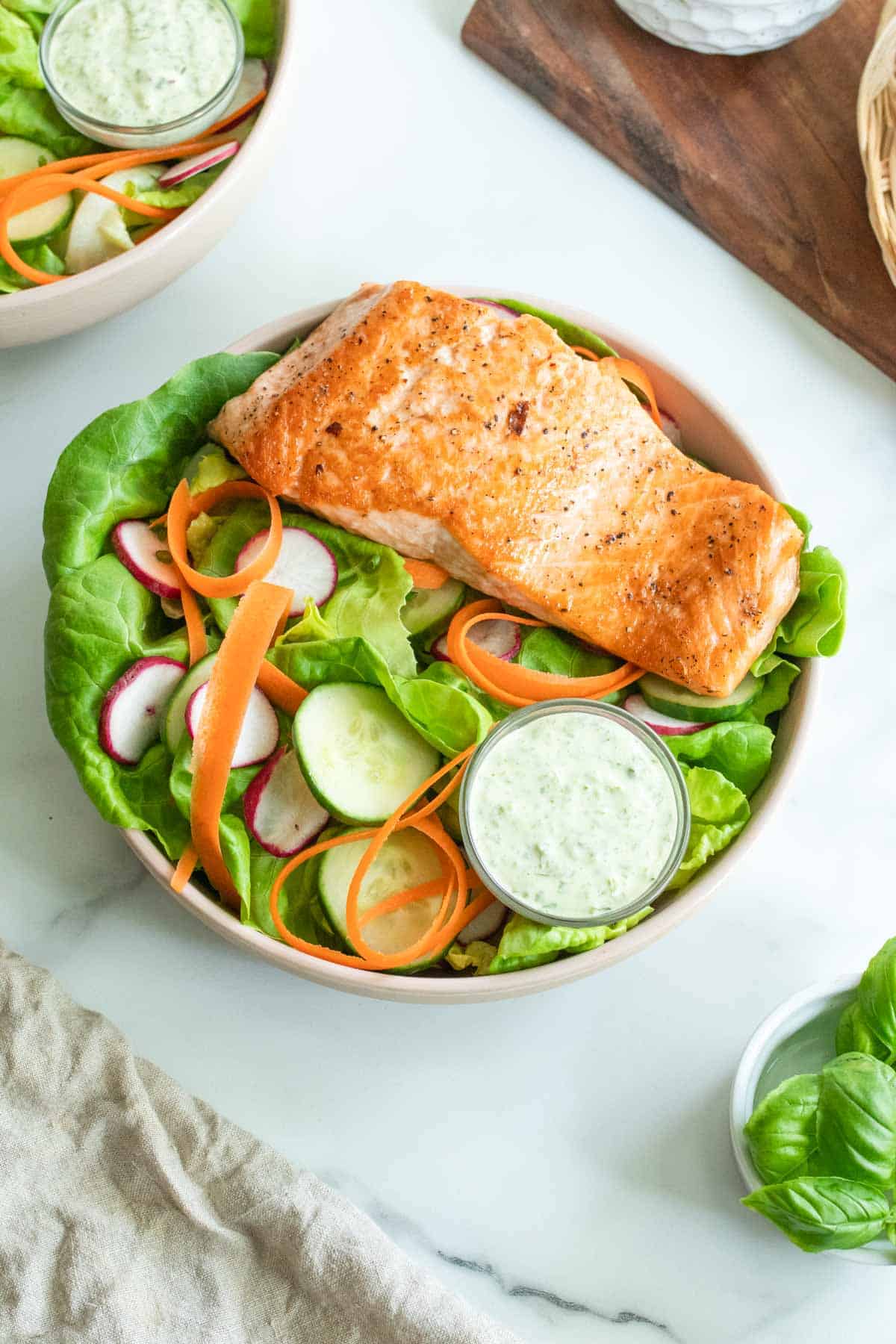 Seared salmon on top of a bibb lettuce salad with carrots and cucumber, next to a wood cutting board.