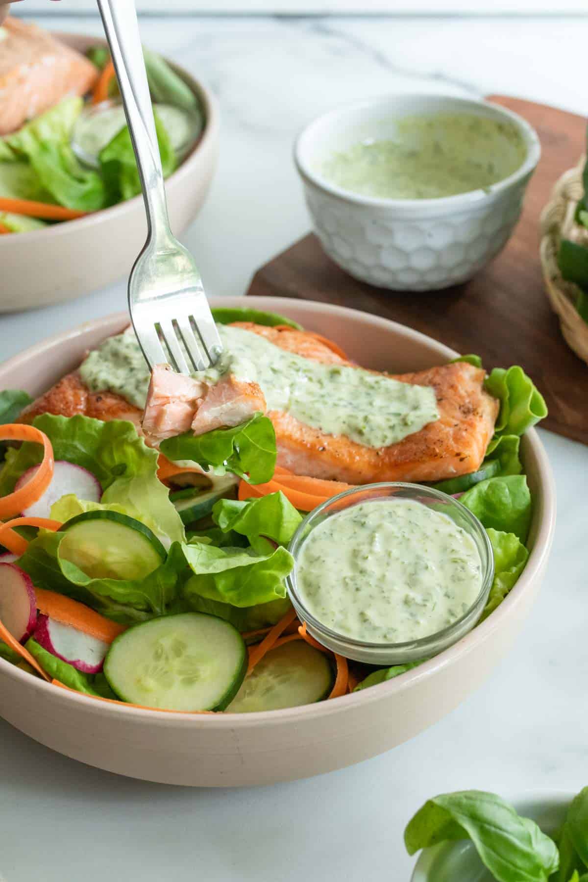 A fork dipping into a salad with cucumbers, salmon, and a creamy dressing.