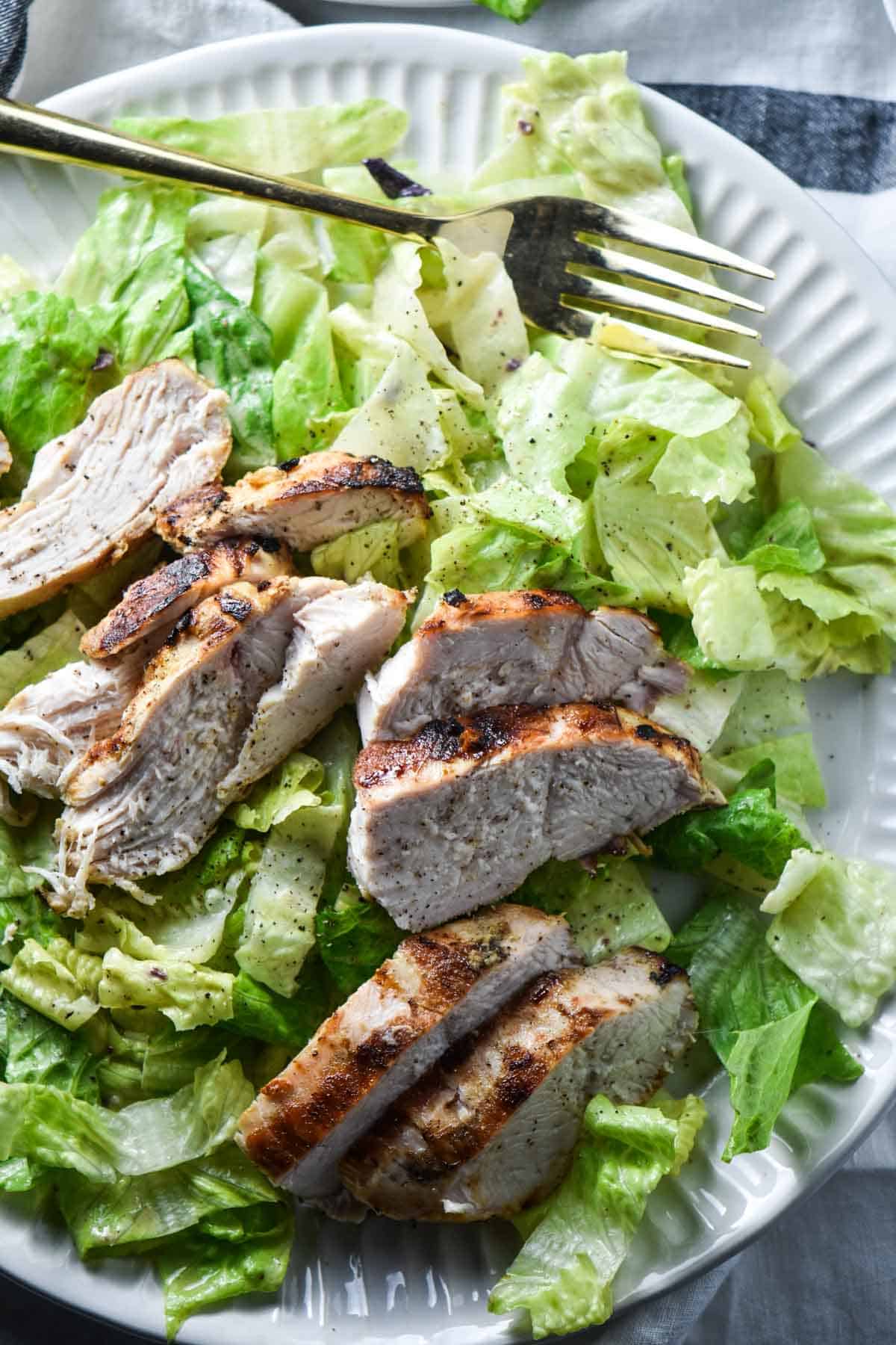 Caesar salad topped with grilled chicken on a serving plate.