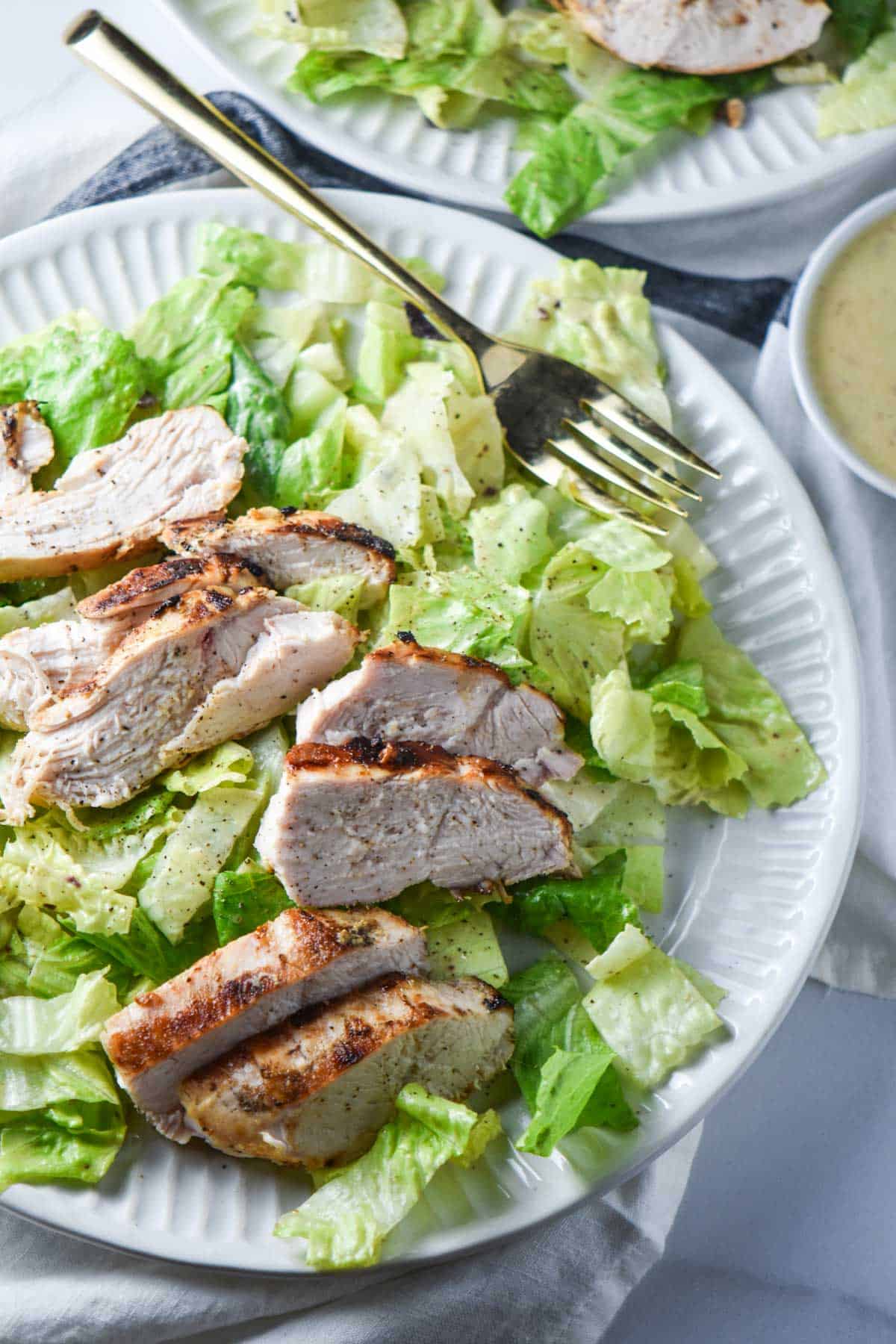 A Caesar salad on a white plate with a gold fork.