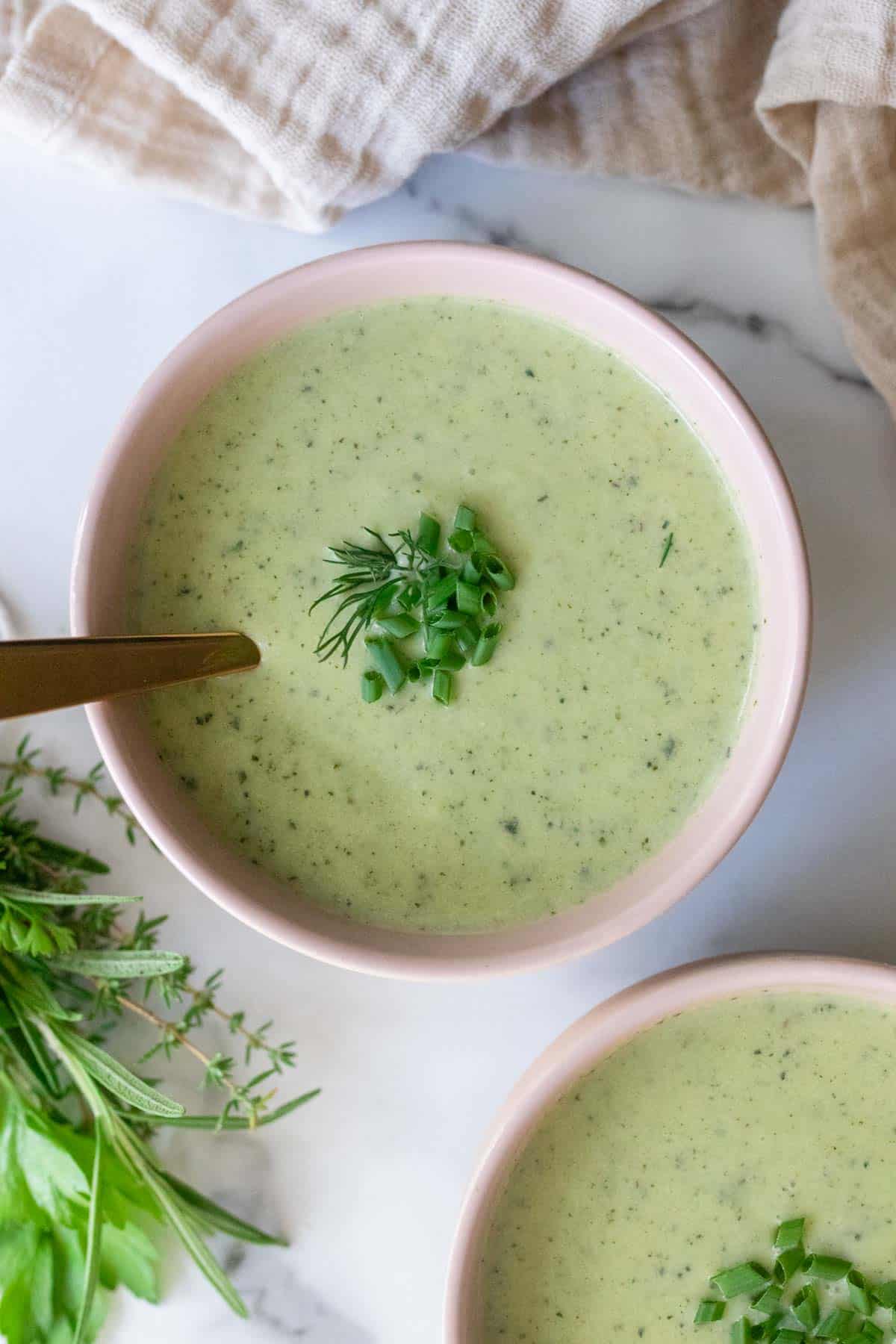 A bowl of green zucchini soup with dill and chives on top.