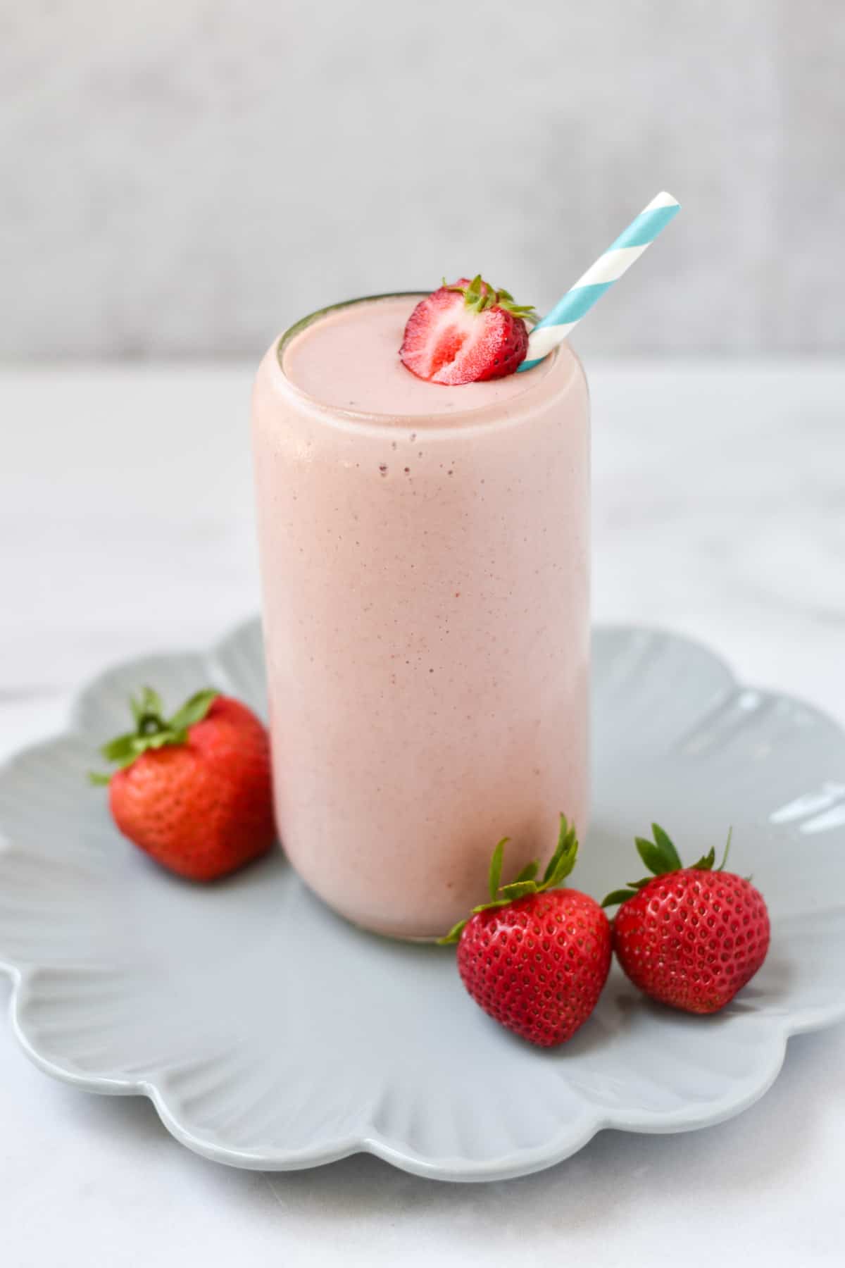 A smoothie with strawberries and cottage cheese on a scalloped plate with a striped straw.