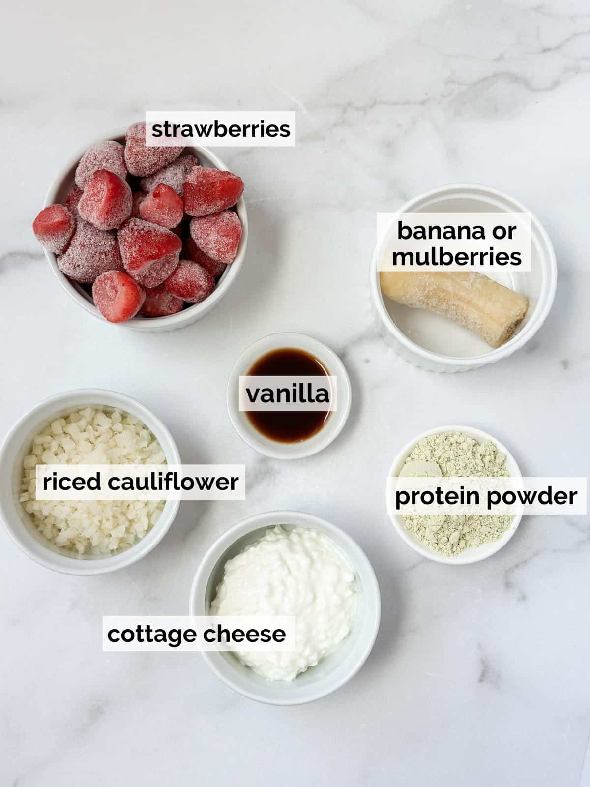 Frozen berries, cottage cheese, vanilla, and protein powder on a marble background.