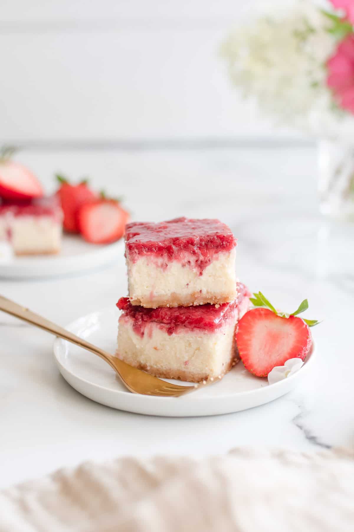 Two cheesecake bars stacked and topped with strawberry compote next to a gold fork.
