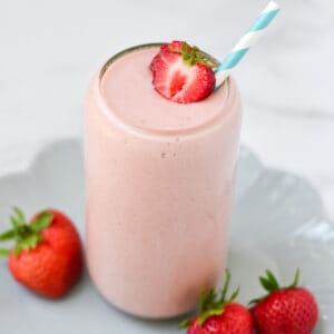 A strawberry cottage cheese smoothie with a blue straw on a plate.