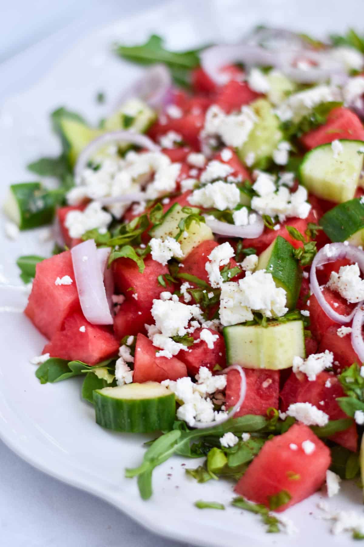 A watermelon basil salad on a white scalloped plate.