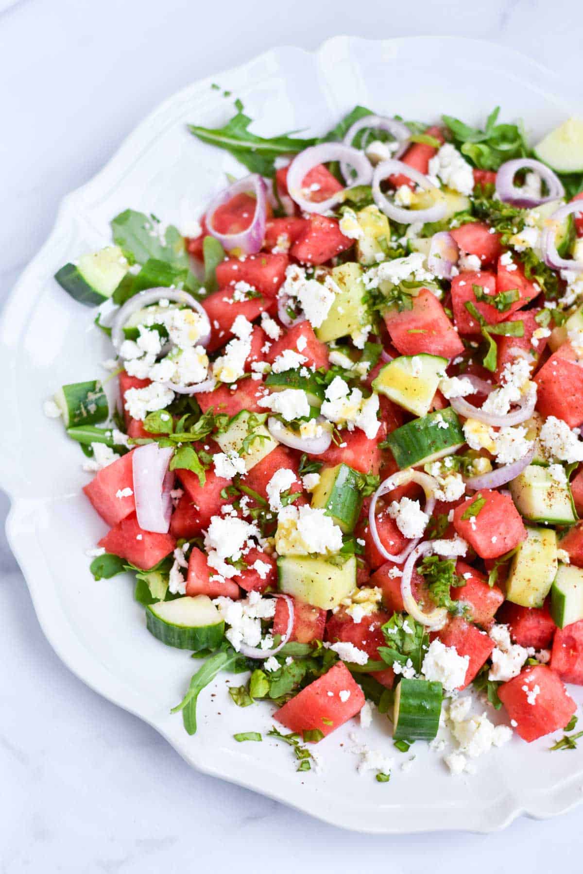 Watermelon salad with arugula on a white scalloped serving plate.