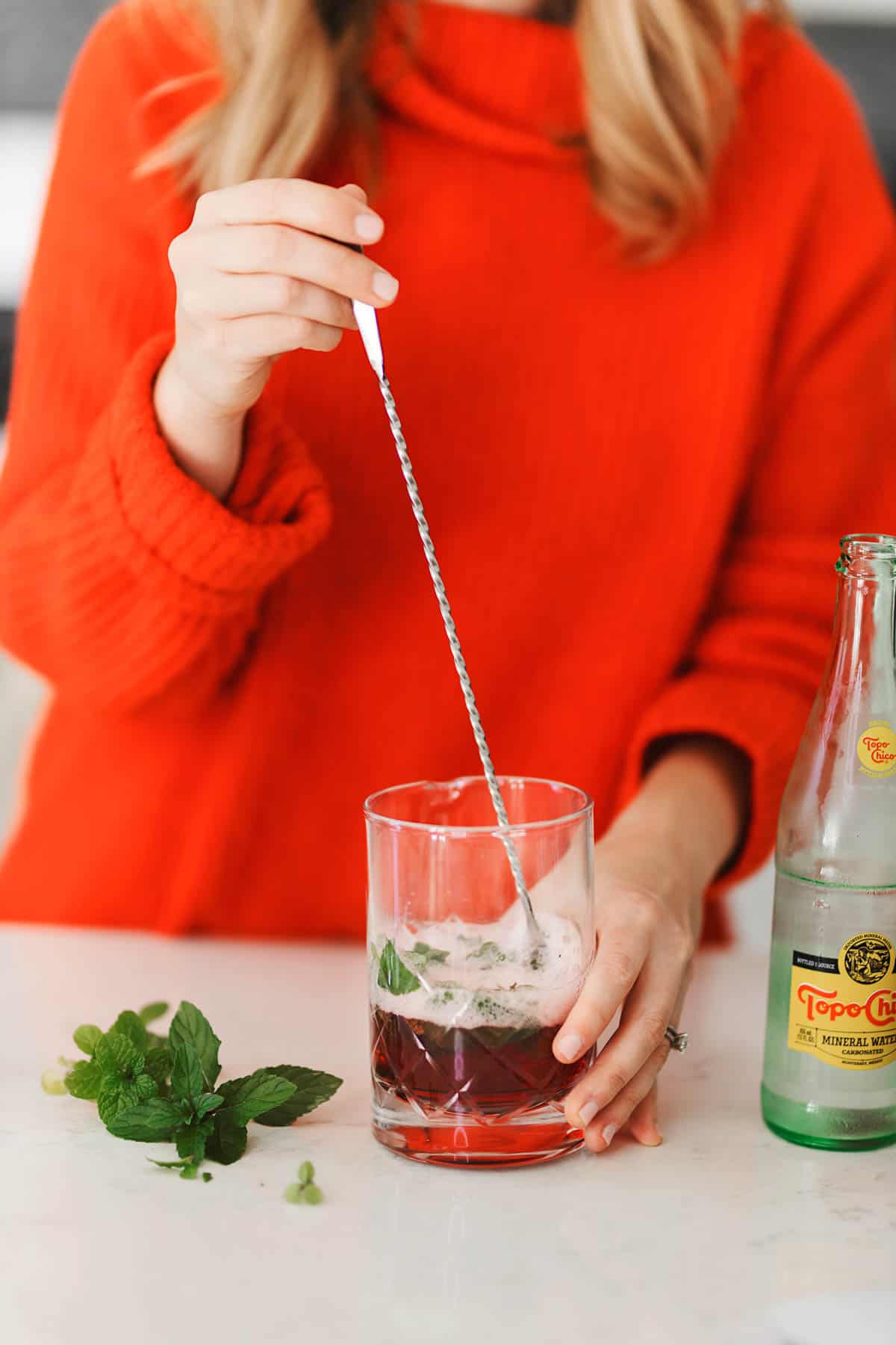 A women in a red sweater using a mixer to stir juice and sparkling water.