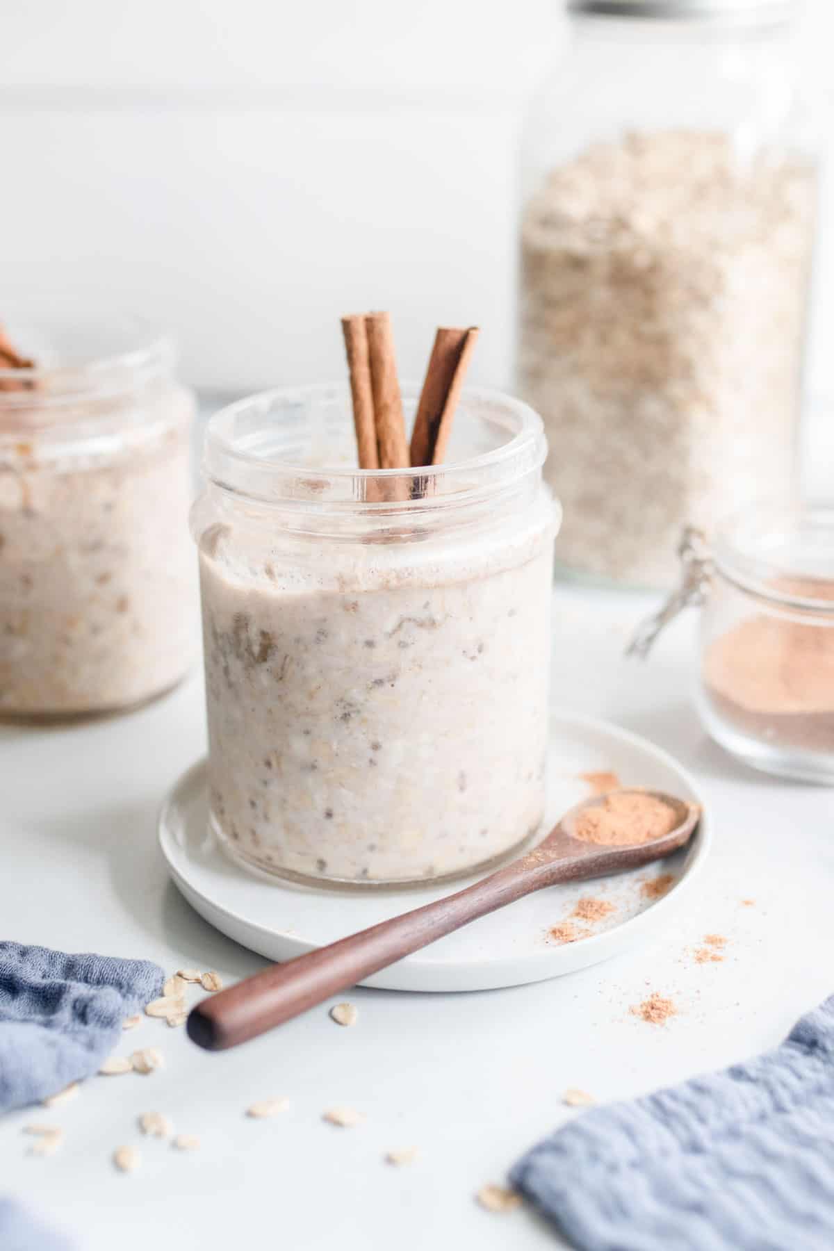 A jar of overnight oats next to a jar of raw oats, with a spoonful of cinnamon sitting in front.