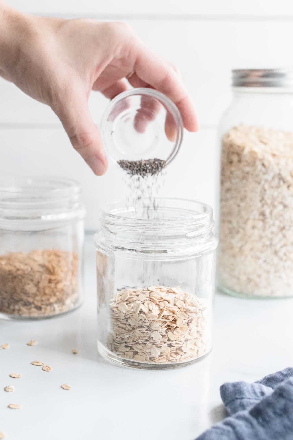 A hand pouring chia seeds into a jar of oats.