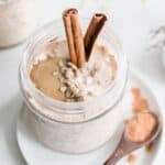 Overnight oats in a jar with cinnamon, seeds, and seed butter next to a spoonful of cinnamon.