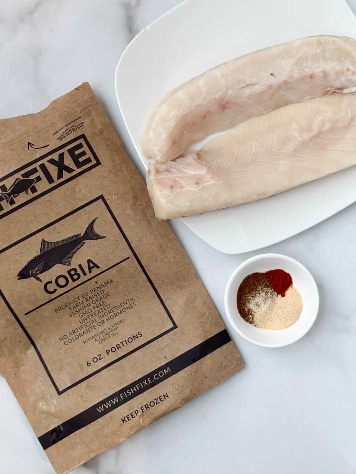 A cobia fish fixe package next to 2 fish fillets and a blackening seasoning.
