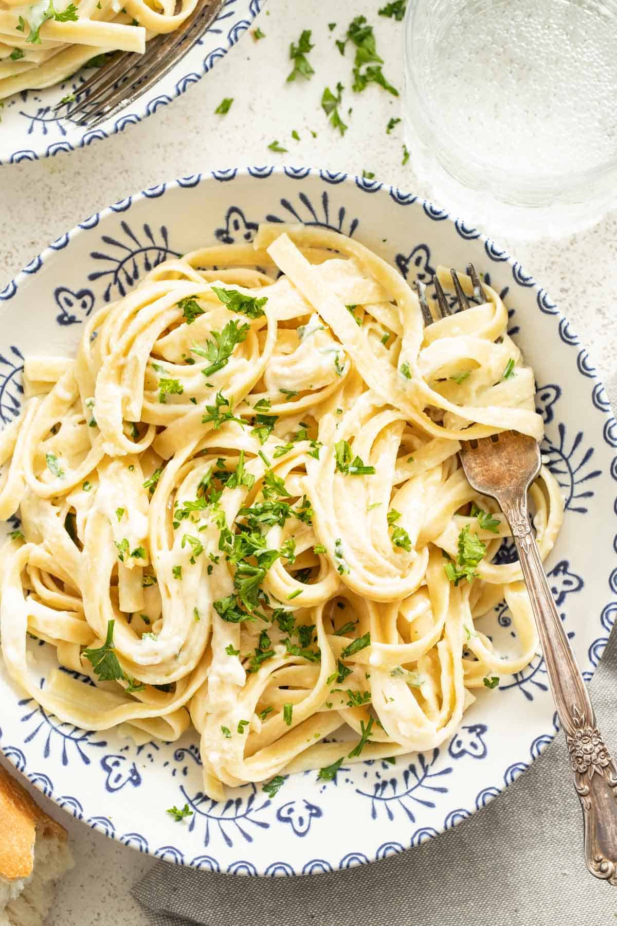 A bowl of creamy pasta topped with parsley and a fork.